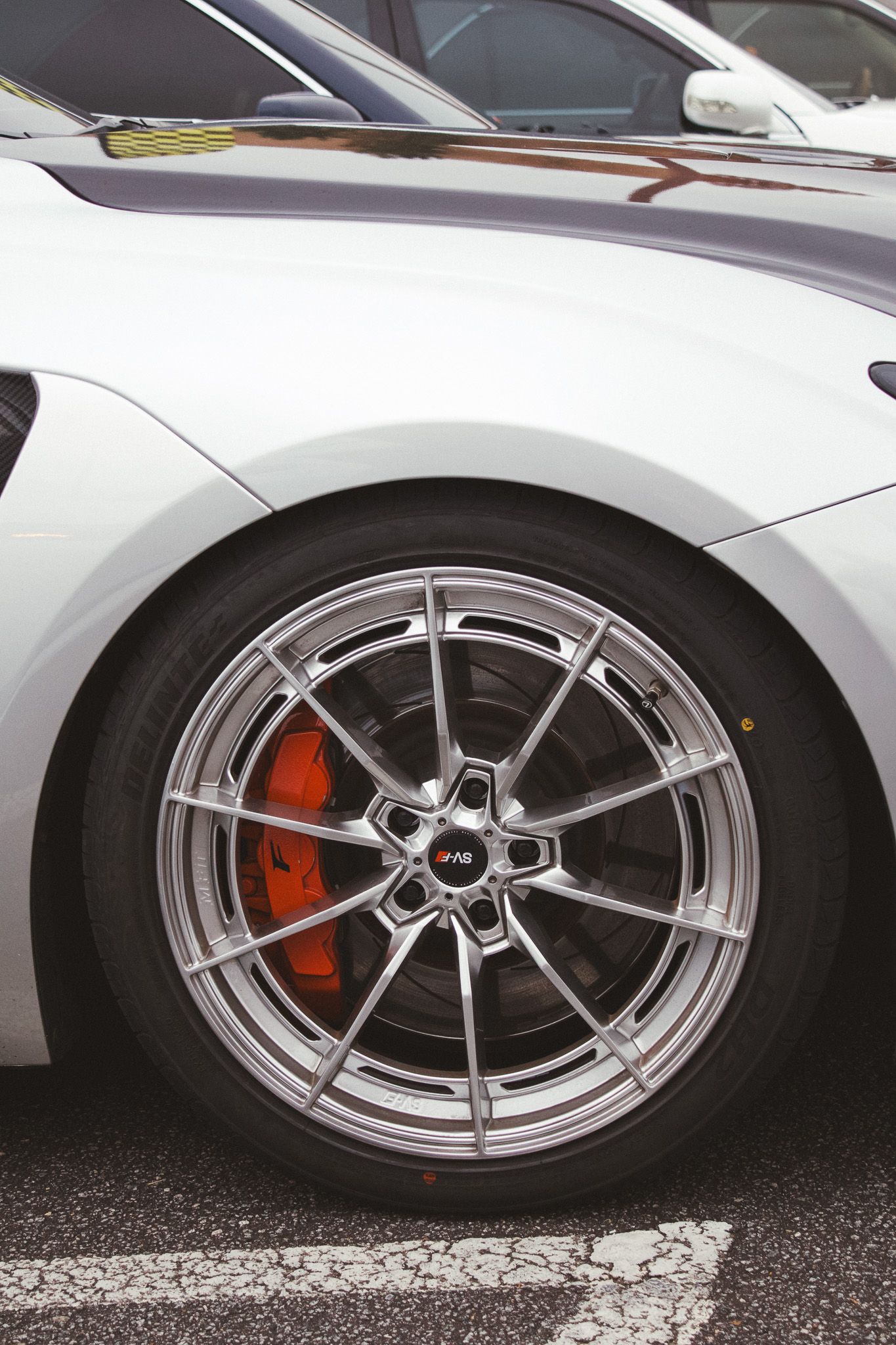 Close up of performance car wheel with red brake caliper and silver multi-spoke design.