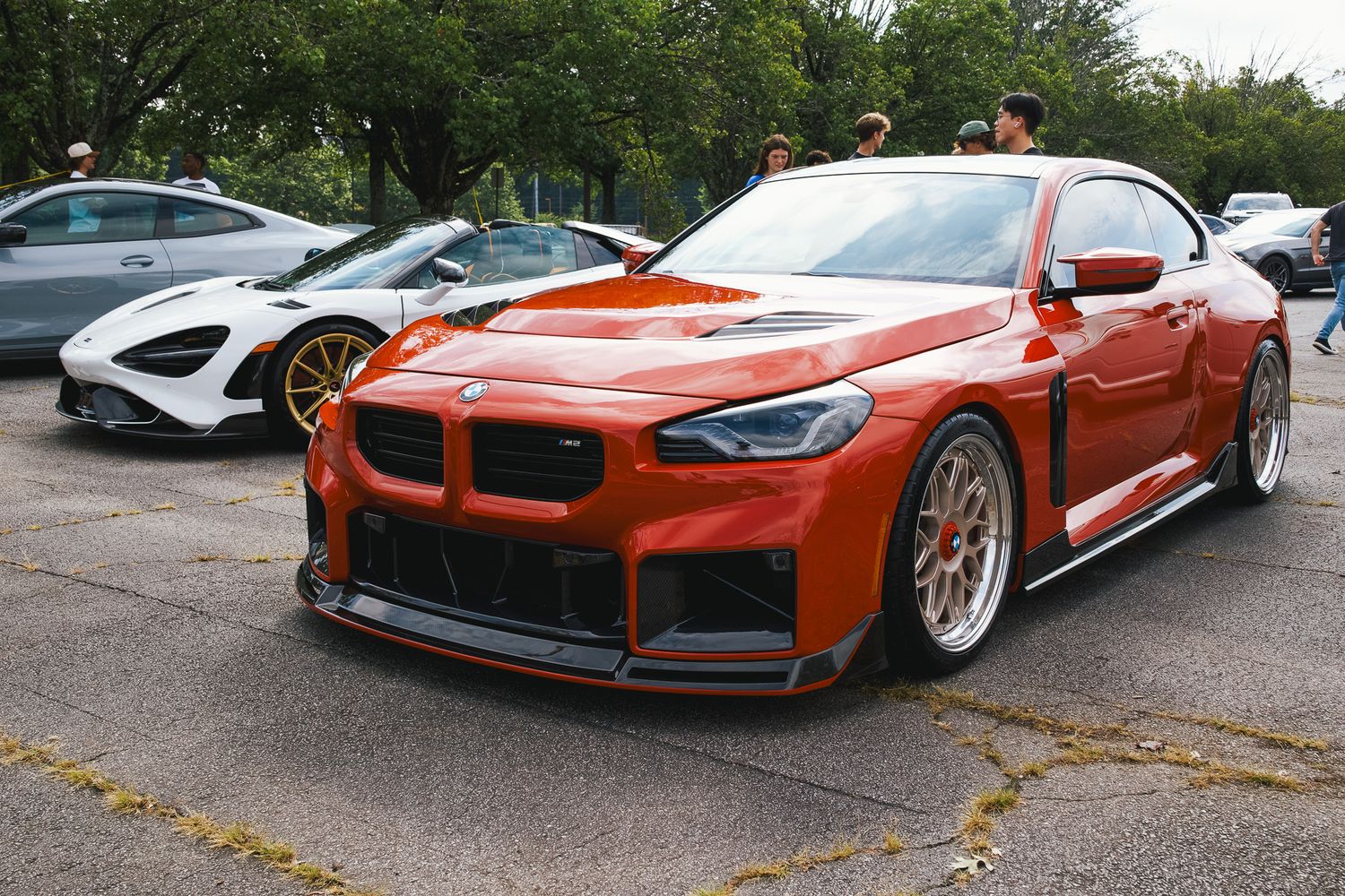 Modified orange BMW M4 with custom body kit and racing wheels at a car show.