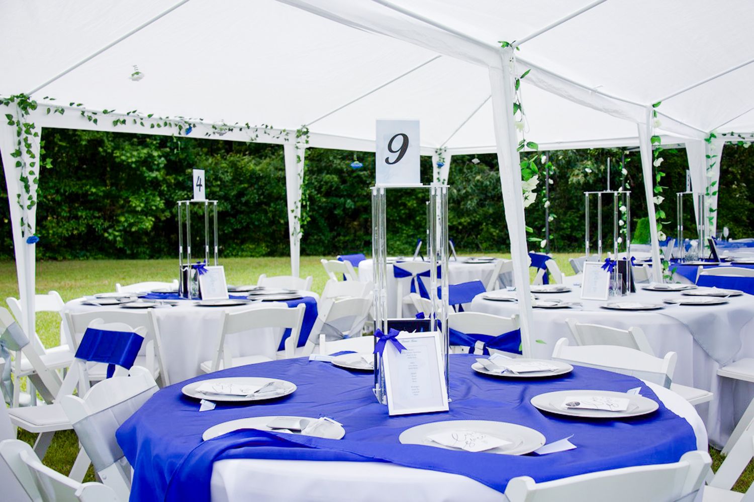 White tent reception setup with round tables covered in royal blue tablecloths and crisp white place settings.