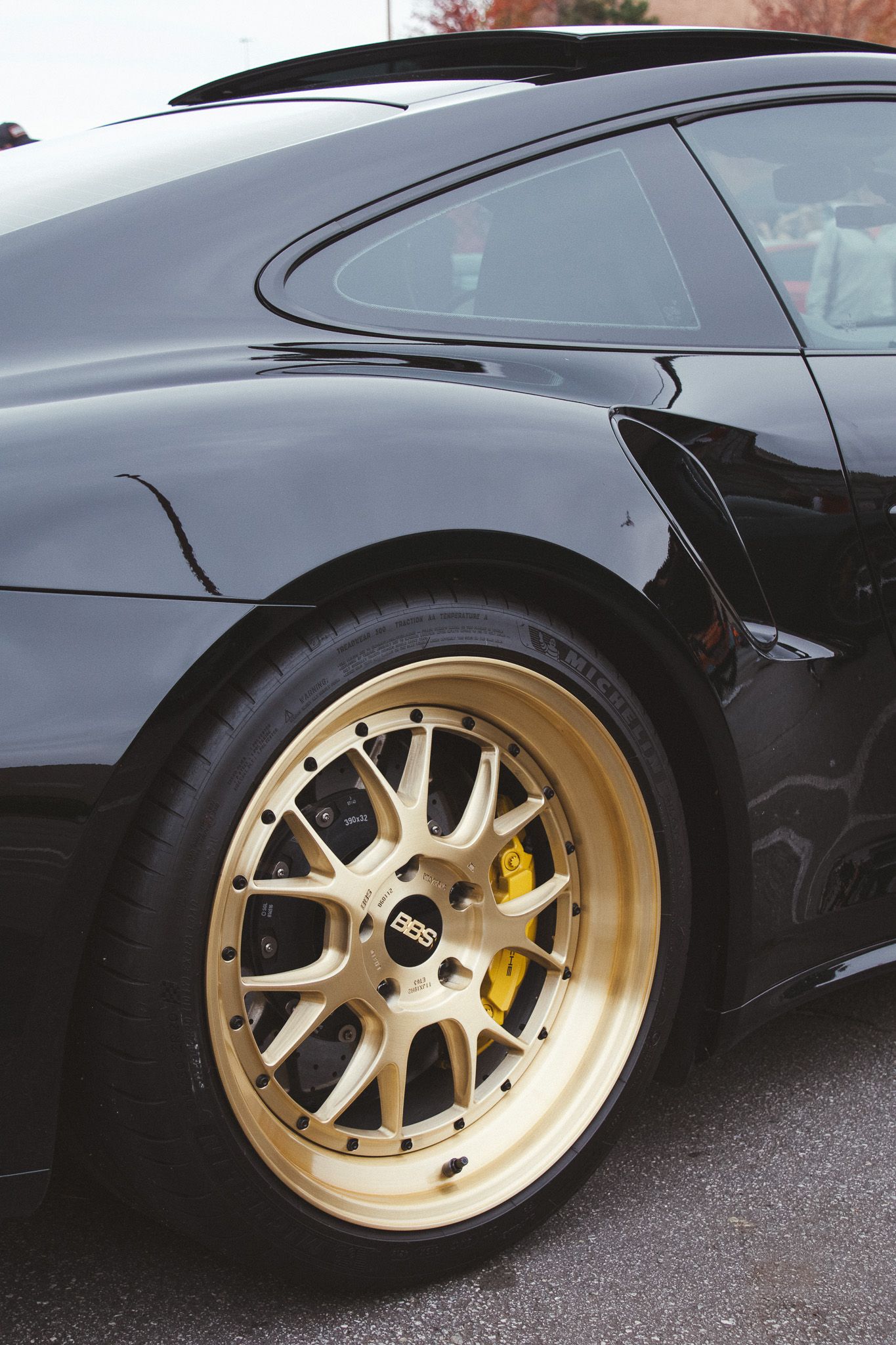 Detail shot of black luxury car with gold BBS wheels and yellow brake calipers.