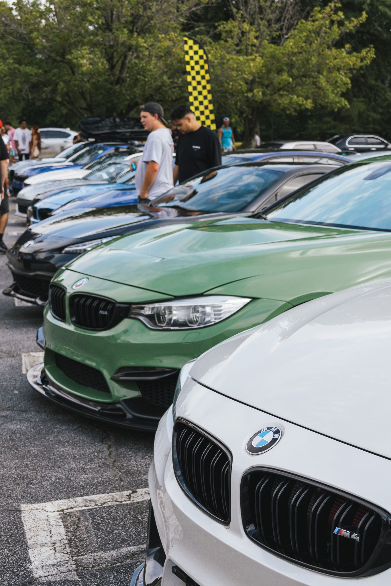 Row of BMW M series cars in various colors at an outdoor car meet.