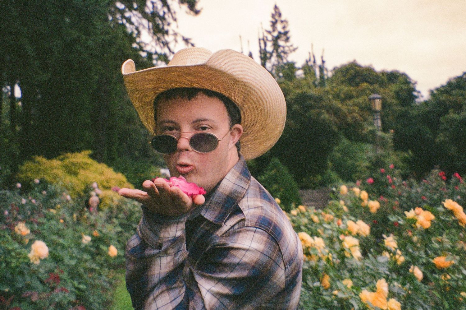 film photo of young man in the Portland Rose Garden blowing rose petals at the camera during a creative portrait session on film