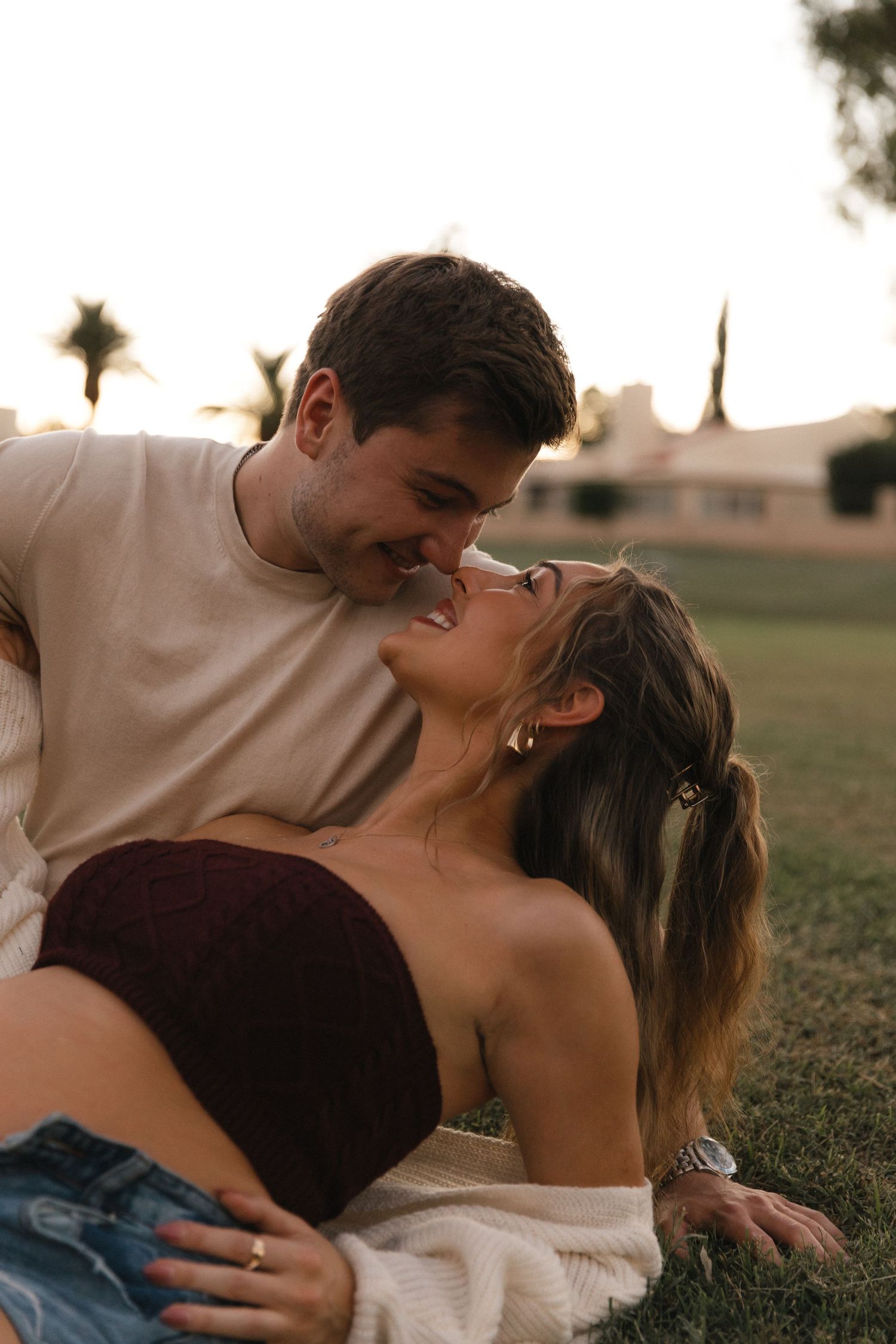 A romantic couple shares intimate moments while lying together on grass at sunset.