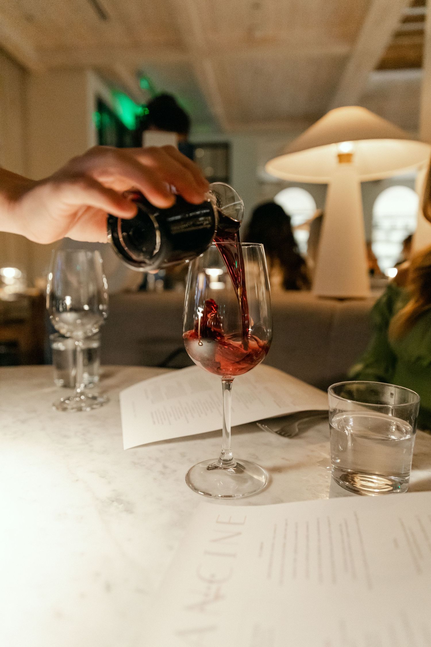 Red wine being poured into a glass on white tablecloth in restaurant setting.