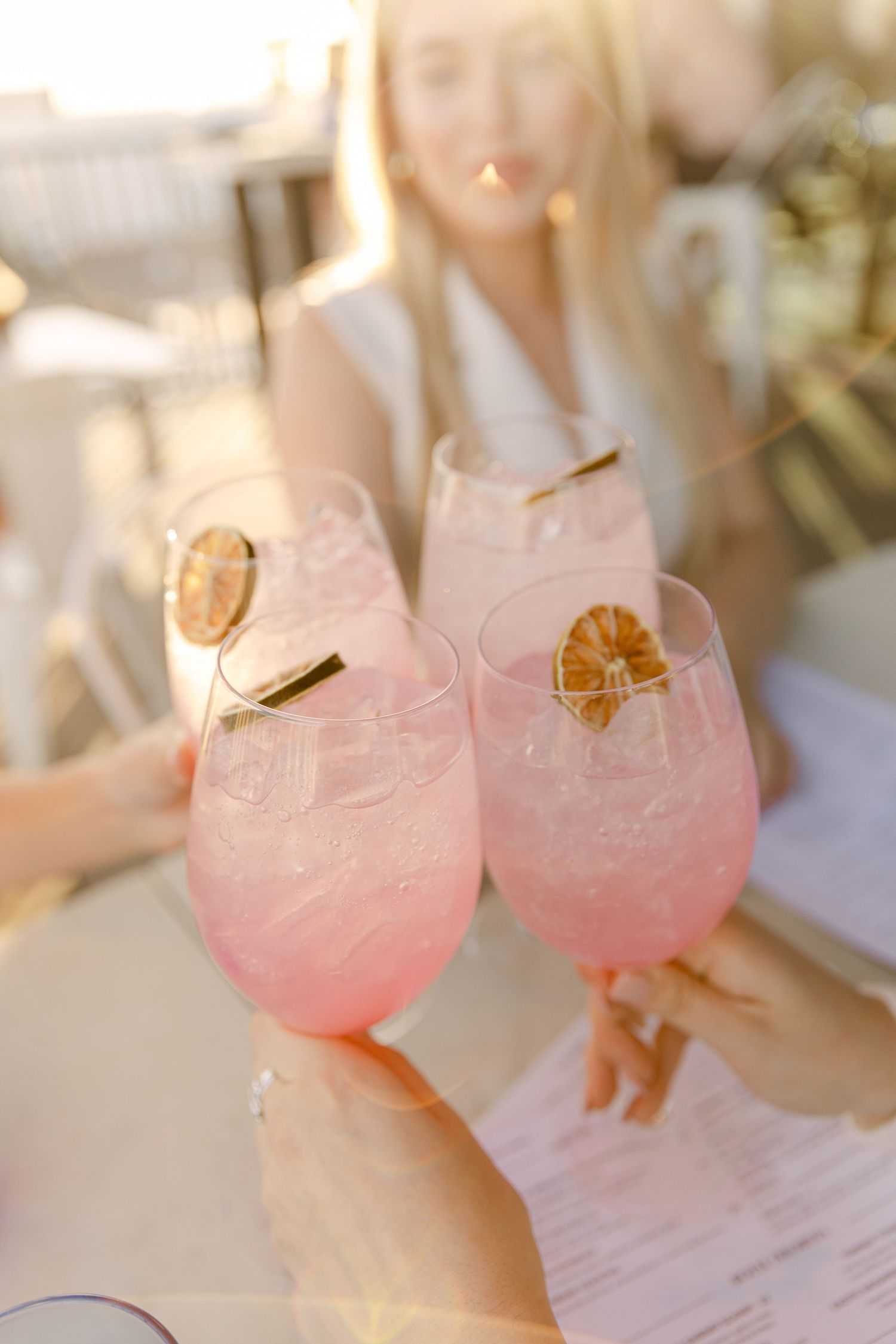 Pink cocktails garnished with citrus and cinnamon sticks in stemmed glasses.