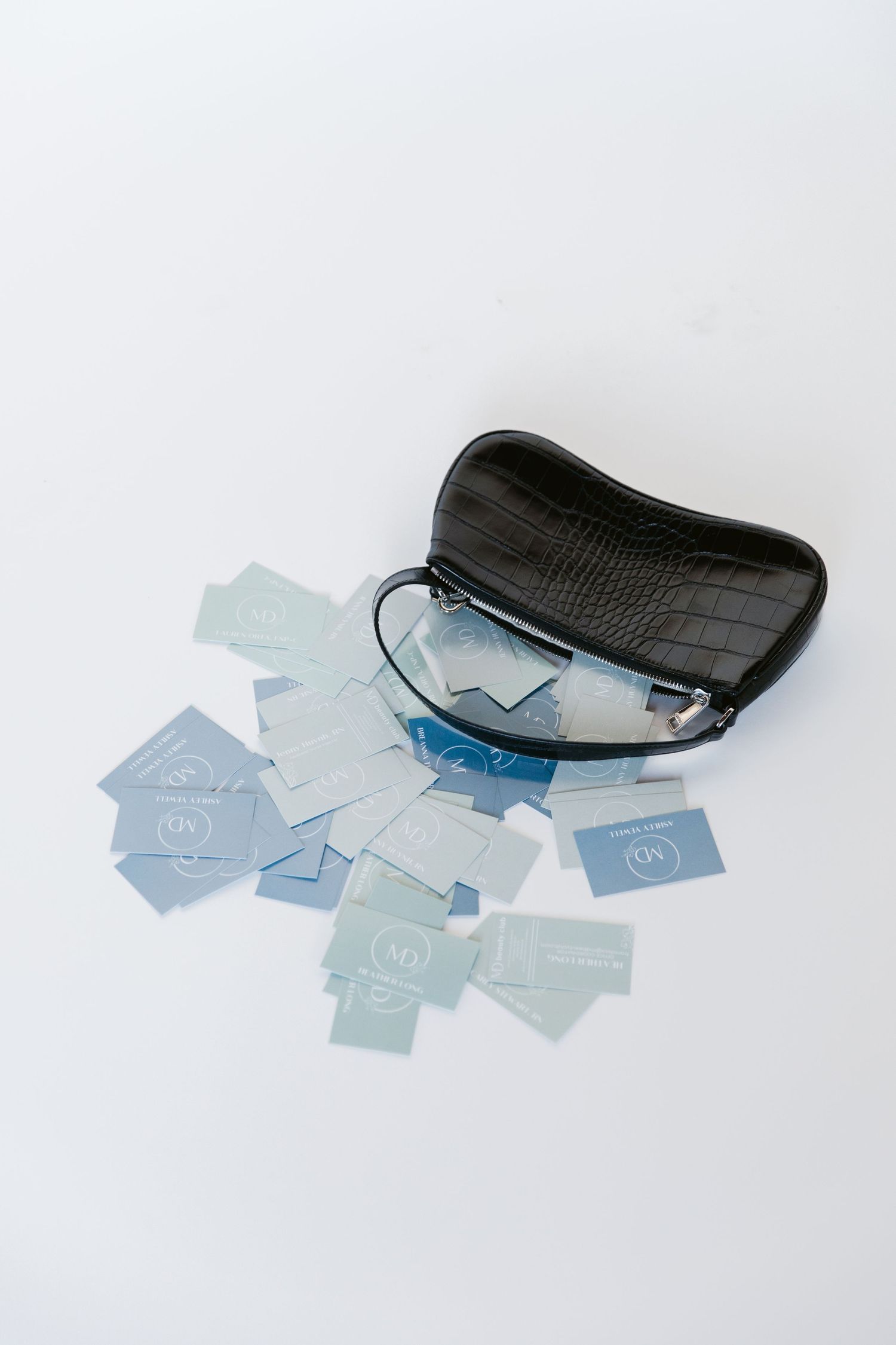 A black leather case with scattered blue and white business cards on white background.