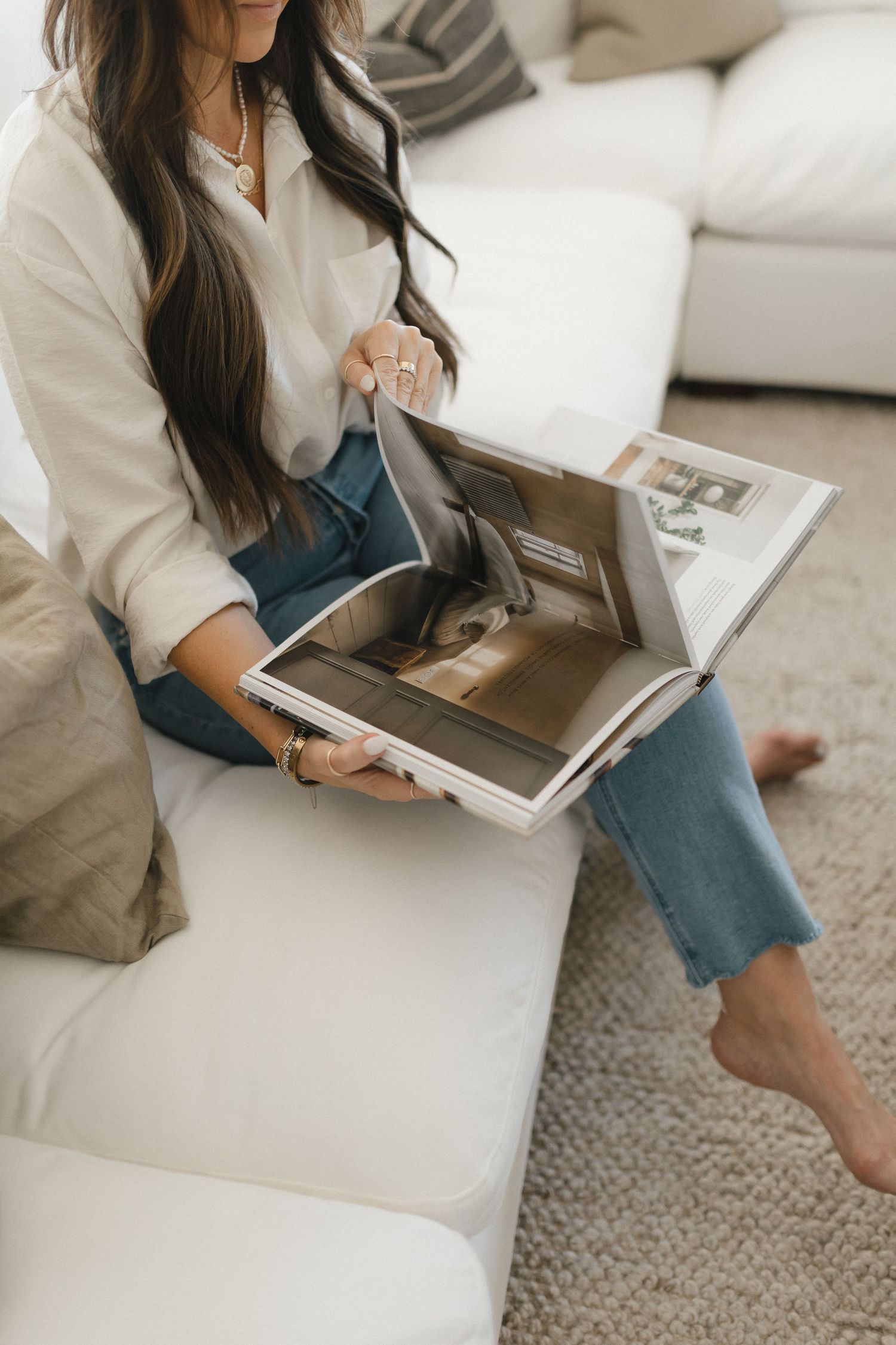 A person in casual attire sits cross-legged on a white sofa while using a laptop computer.