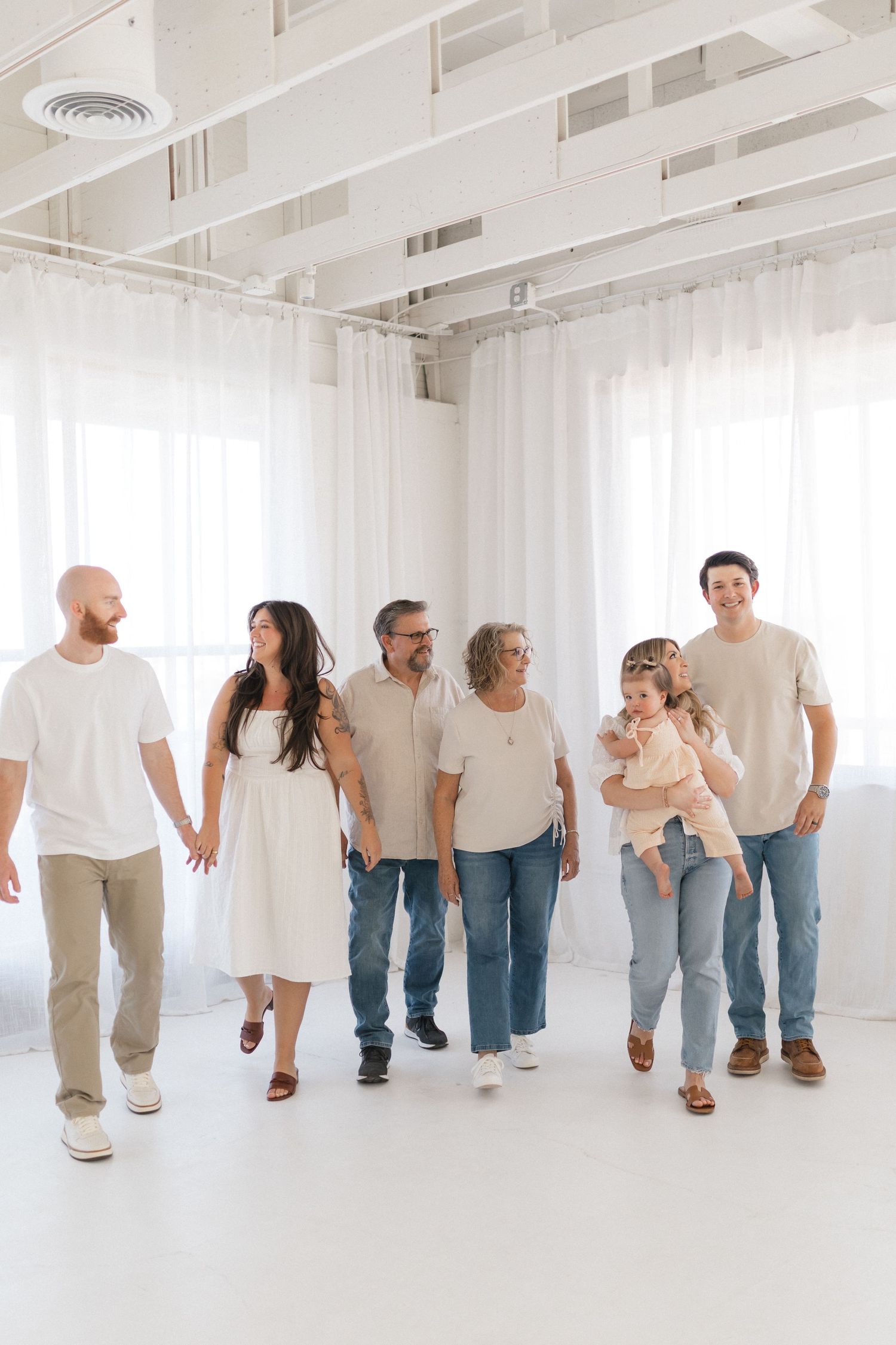 Family members wearing coordinated white and neutral outfits walk together in a bright modern indoor space.