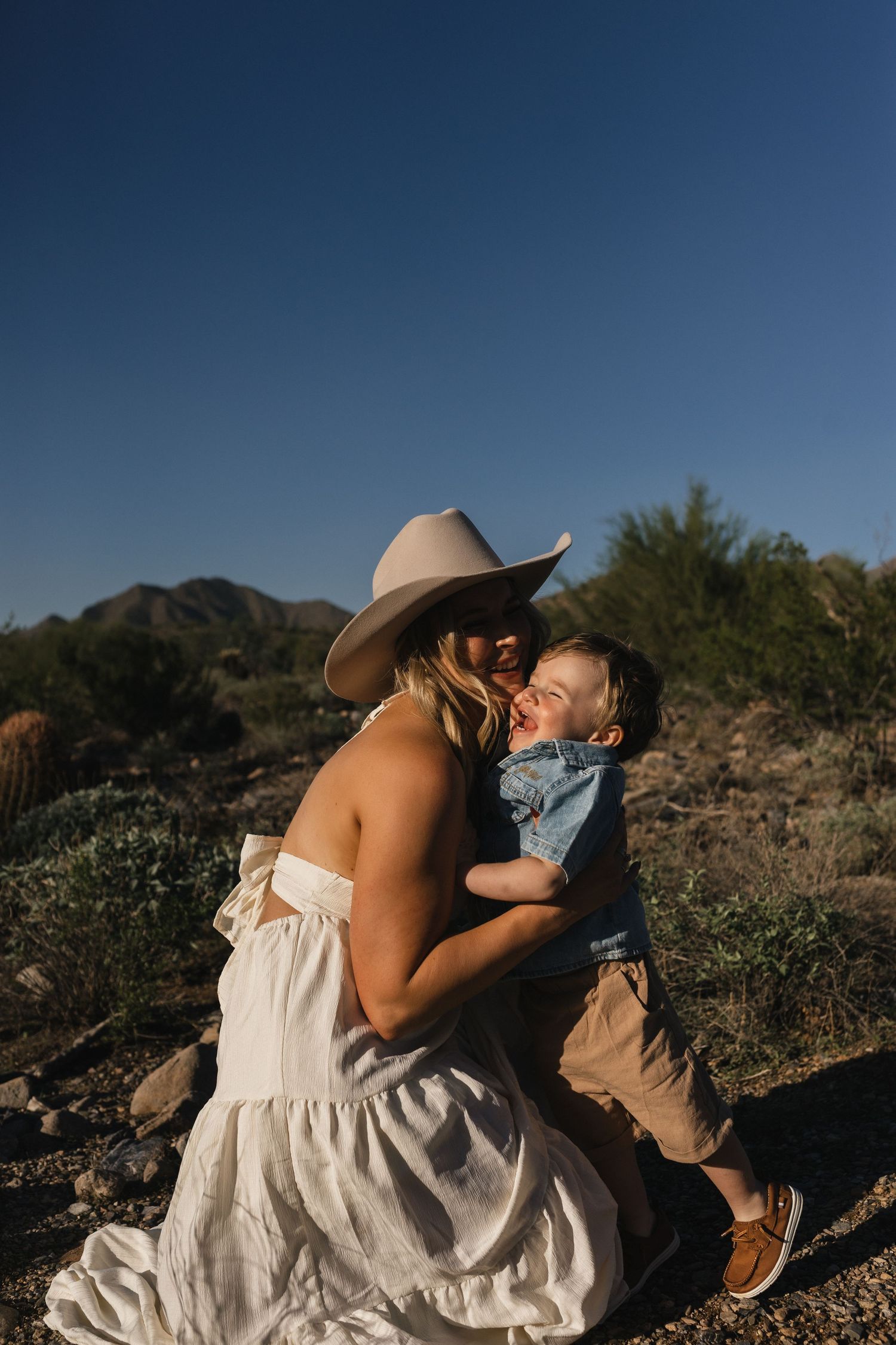 A couple embraces intimately against a desert mountain backdrop during a romantic photoshoot at sunset.