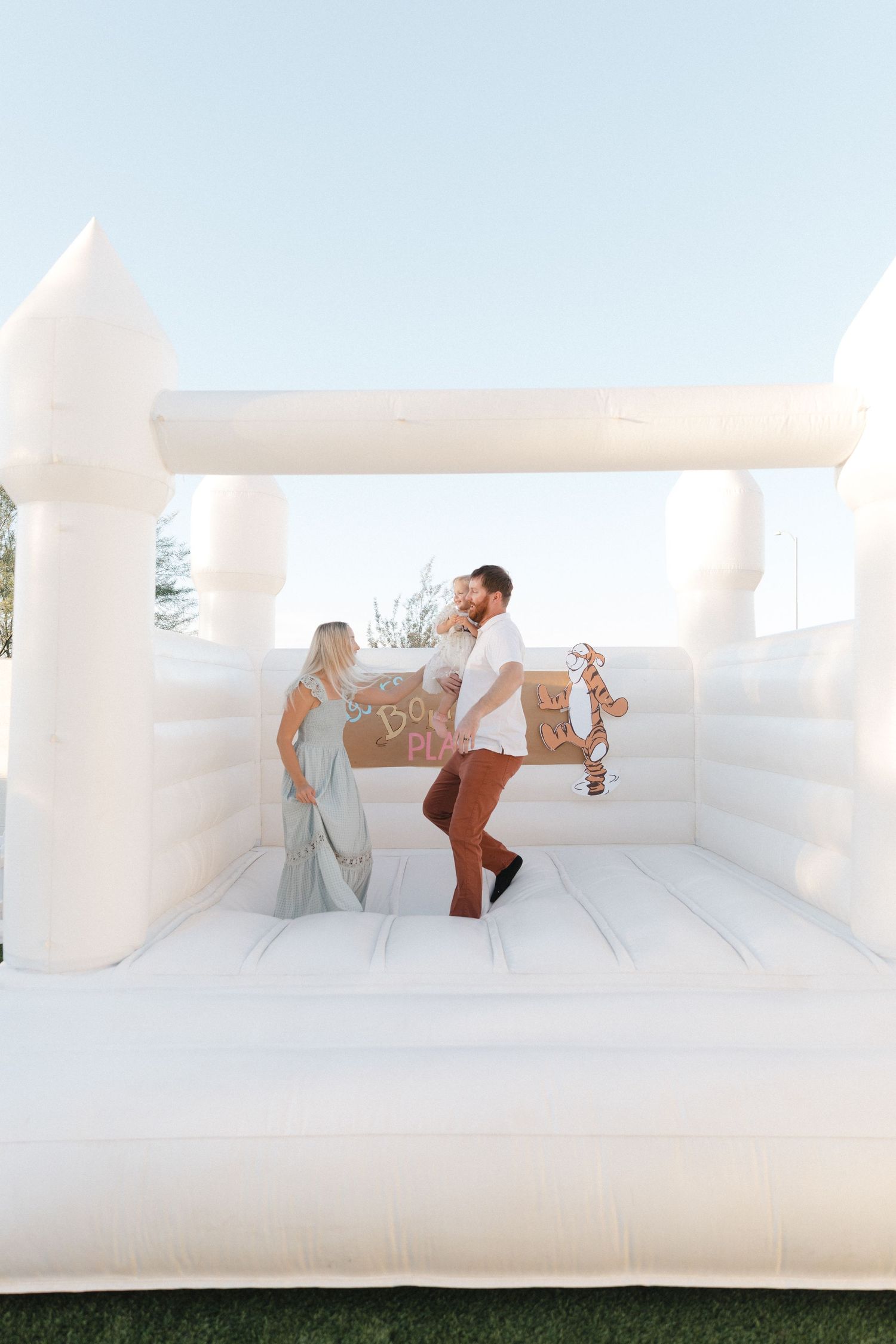 People enjoying themselves while jumping and playing in a white inflatable bounce house on a sunny day.