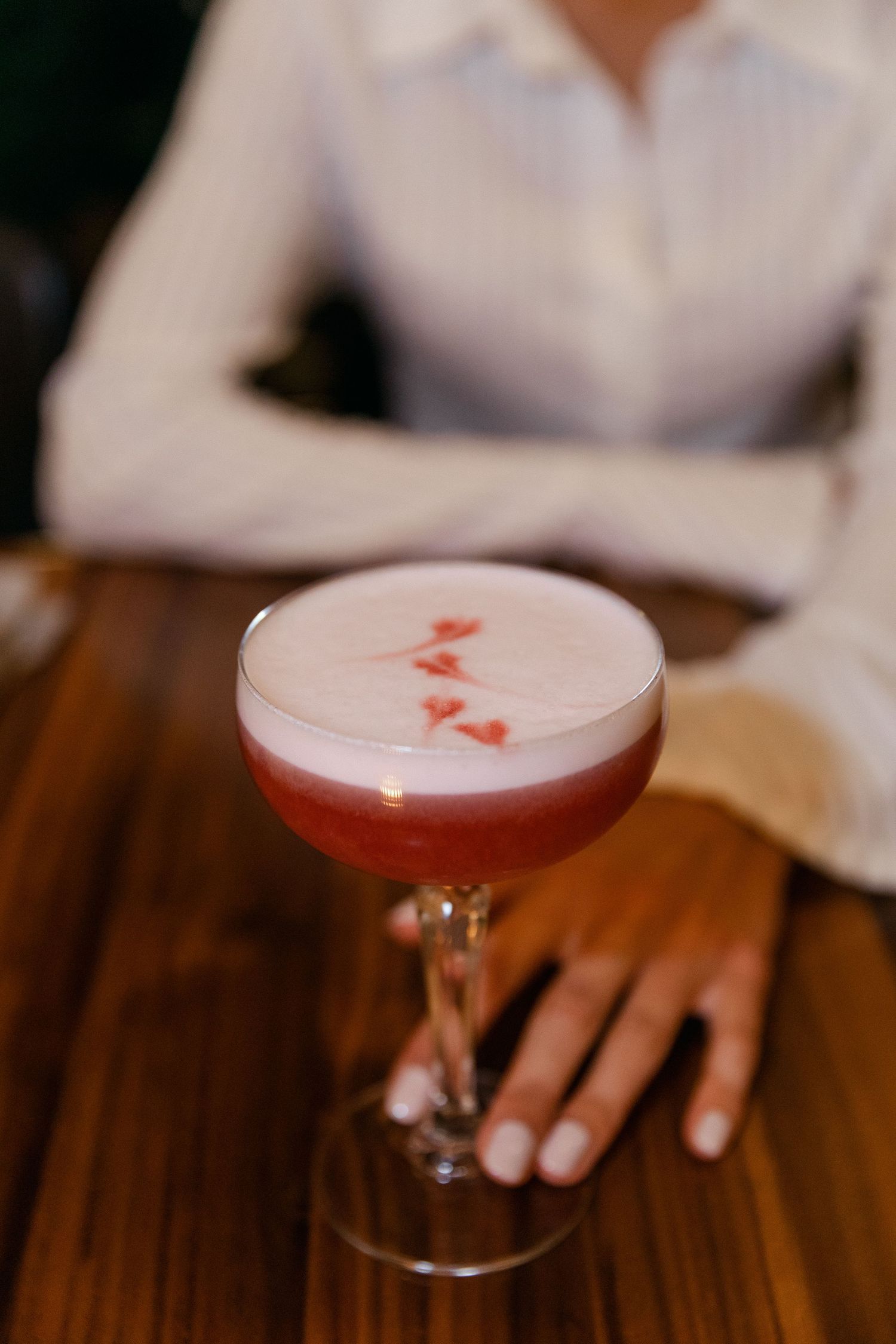 Pink cocktail with floral garnish served in a coupe glass on wooden surface.