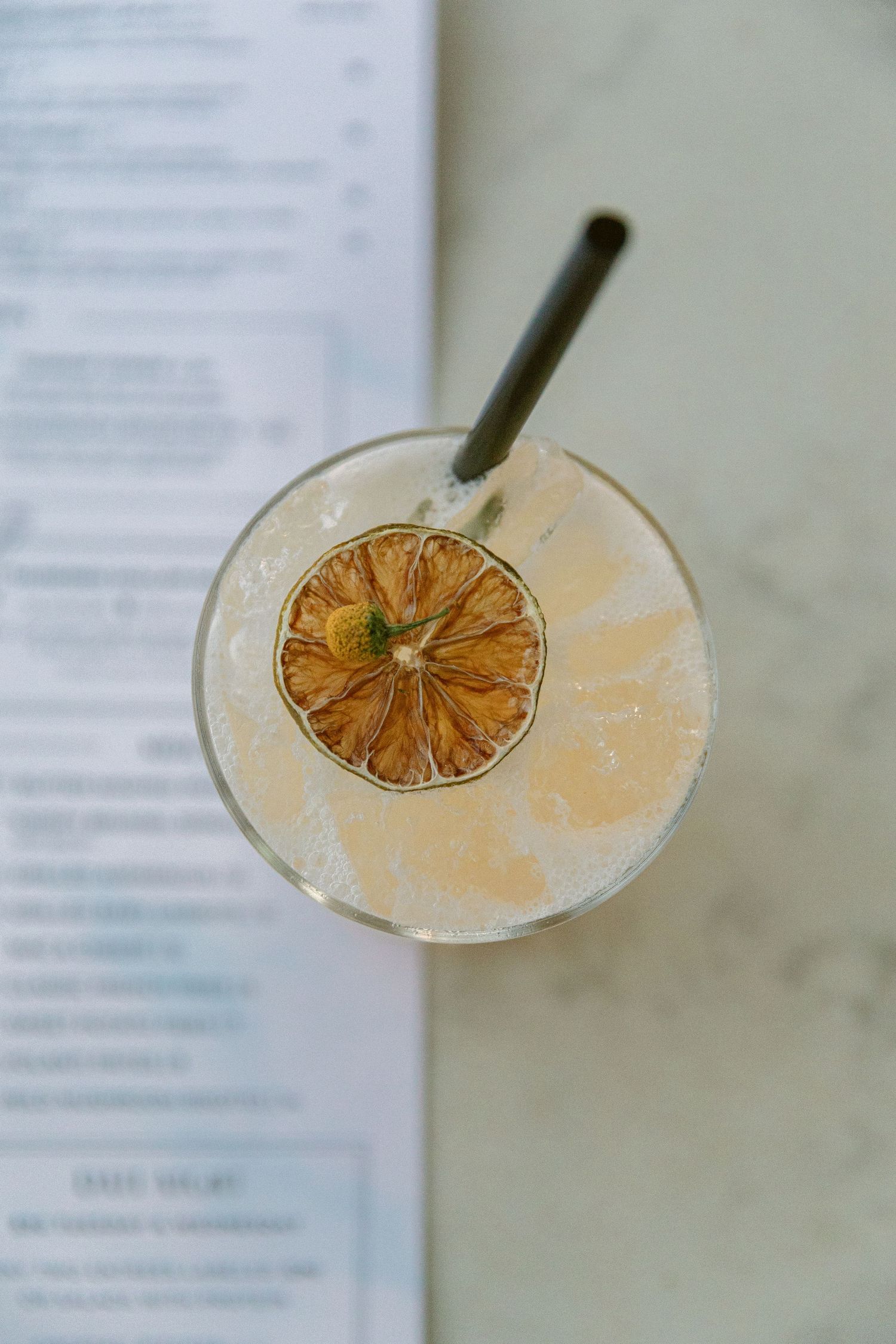 A refreshing cocktail garnished with a dried citrus wheel and straw in a glass, viewed from above.