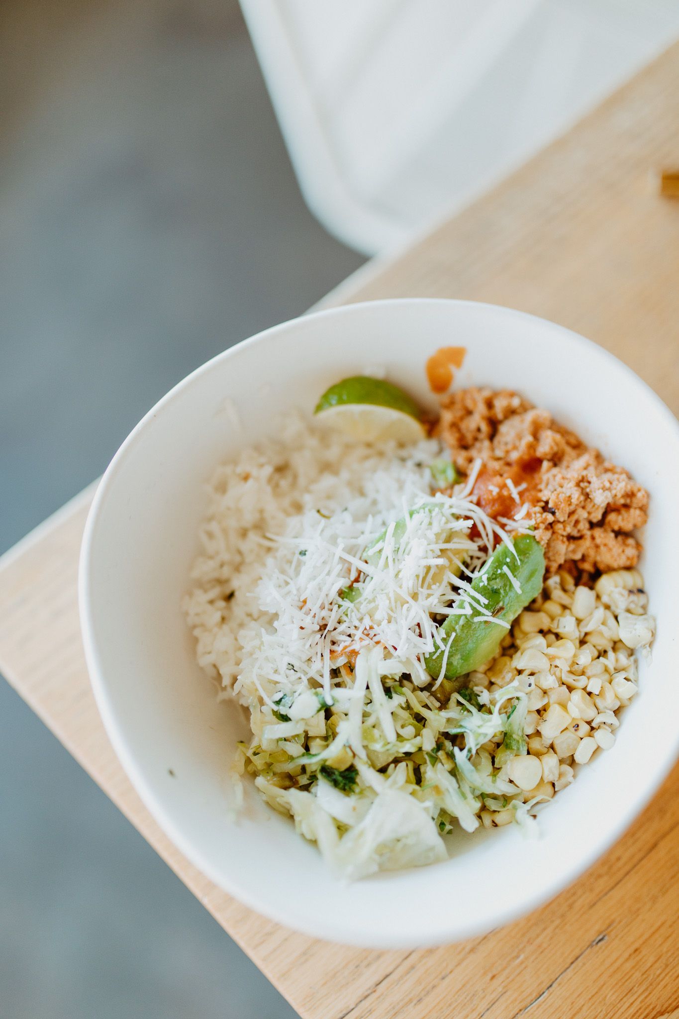 Rice bowl topped with shredded cheese, microgreens, and seasoned meat.