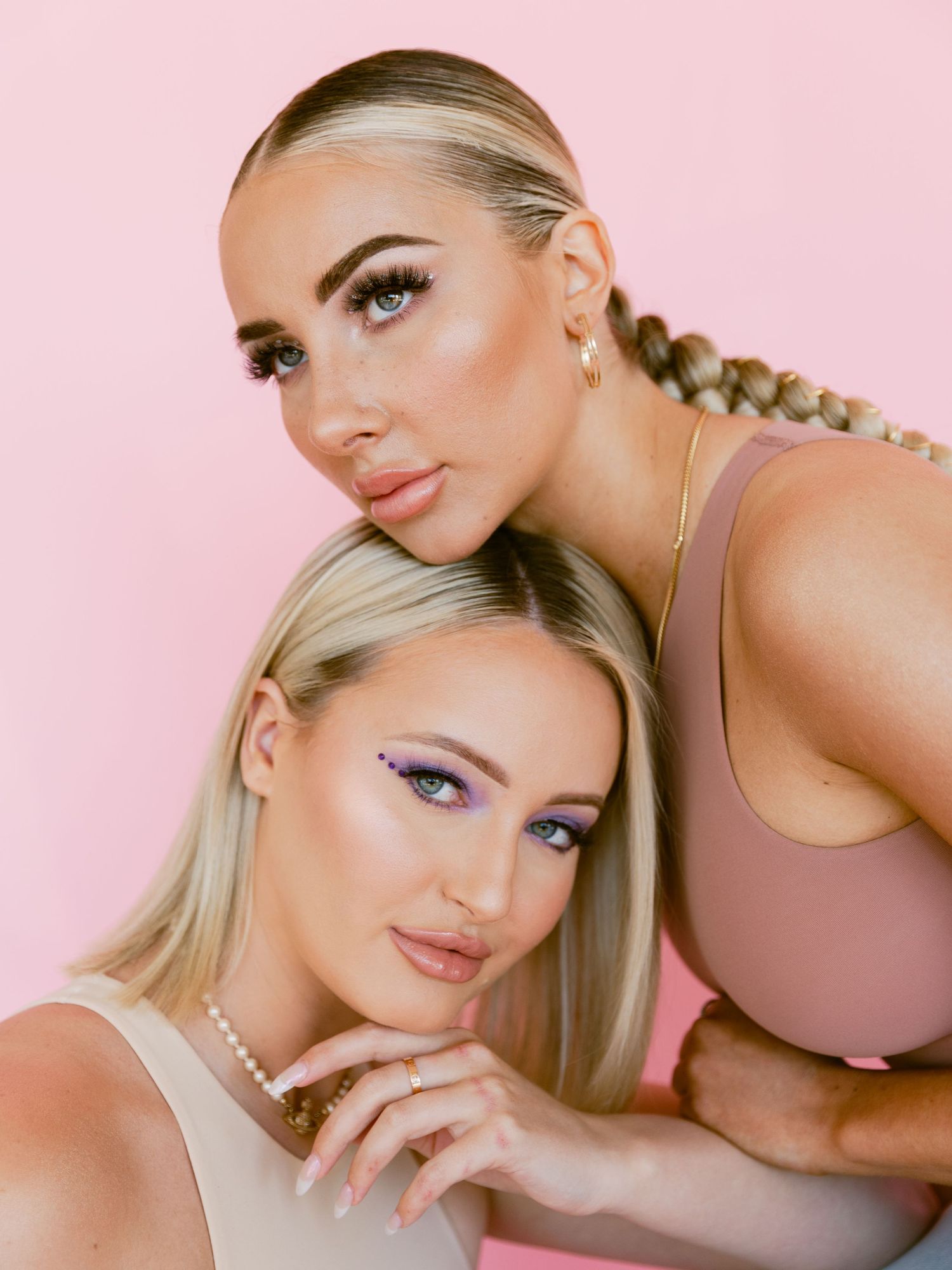 Beauty portrait of two models with glamorous makeup against pink backdrop.