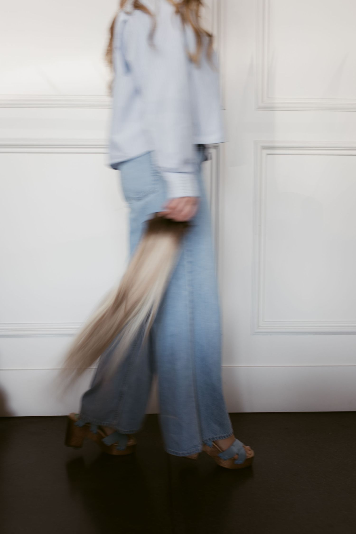 Motion-blurred fashion photograph showing person in flowy light blue outfit with wide-leg jeans and platform shoes walking.