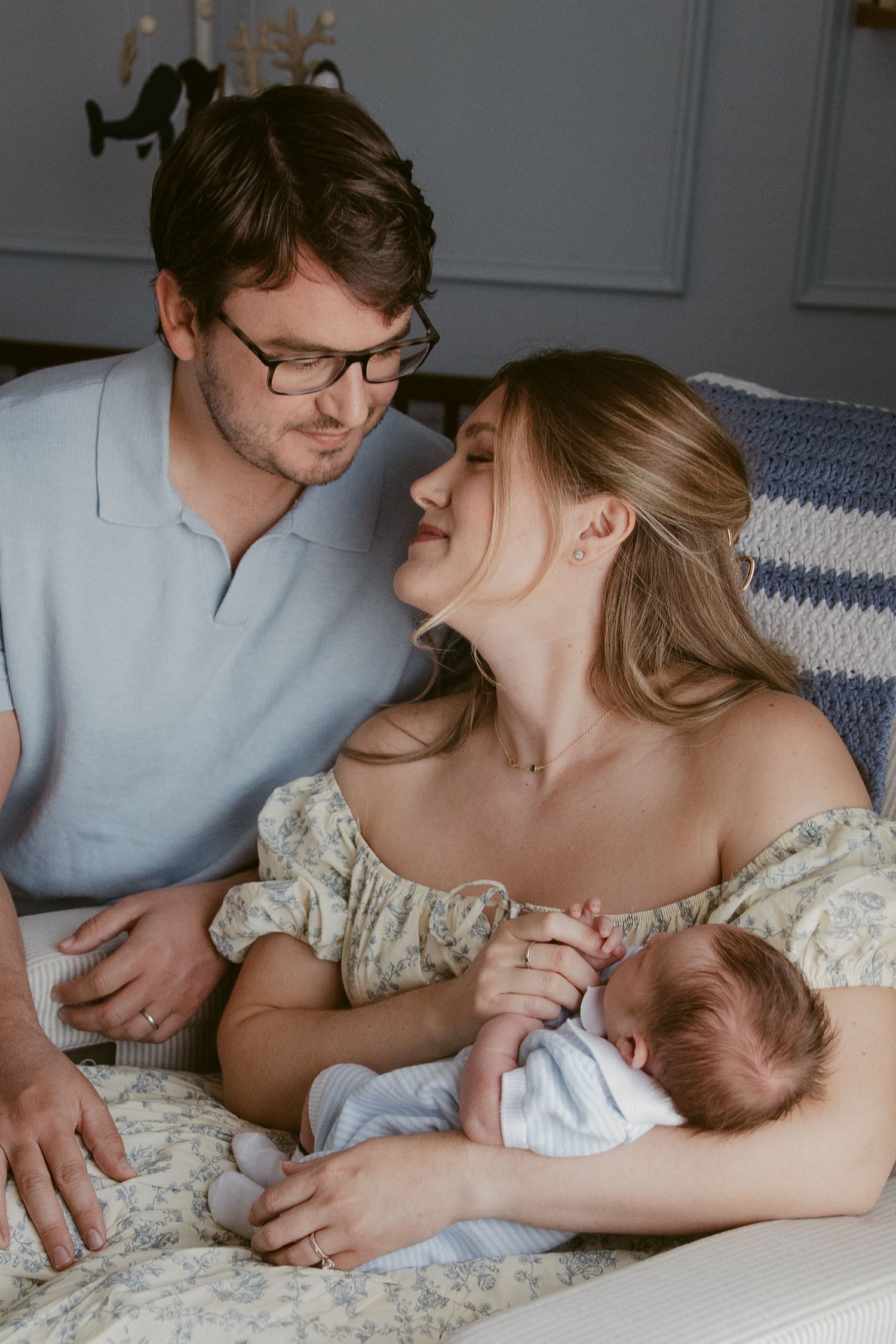 A couple sits together on a couch with their newborn baby in a cozy home setting.