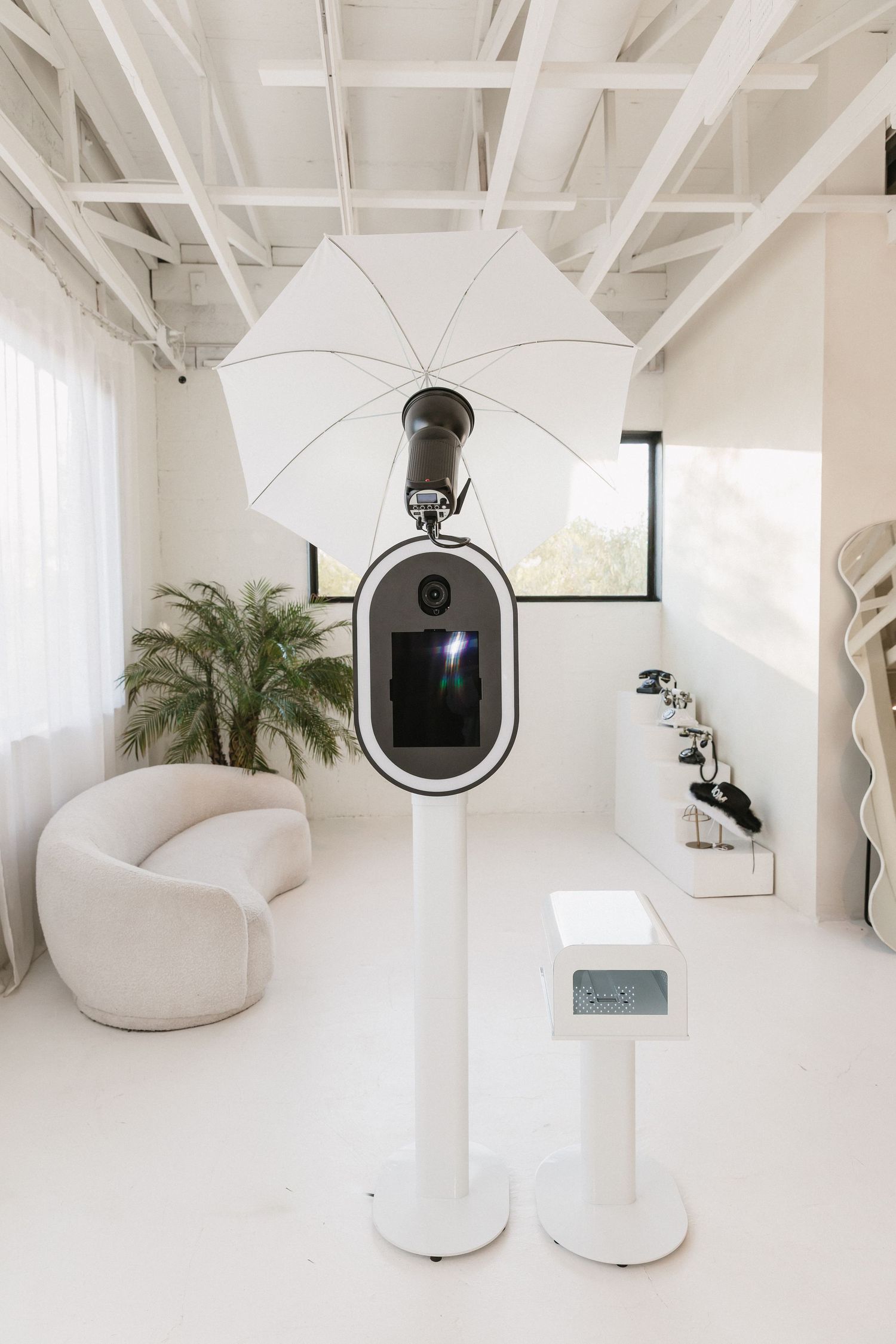 Modern minimalist white office space with exposed beams, sleek furniture, and potted plants creating a clean workspace environment.