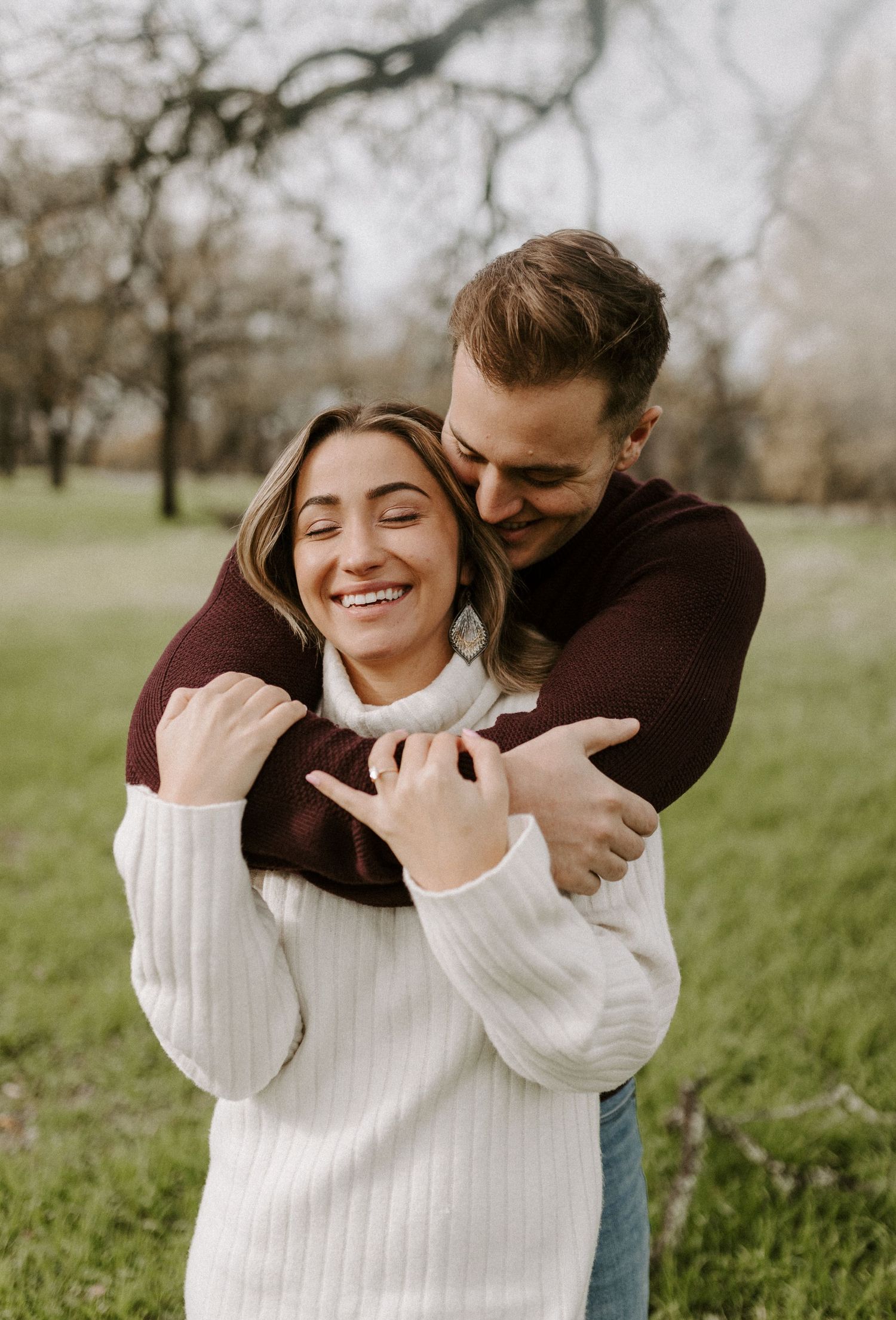 A couple in sweaters sharing a joyful embrace in a park setting.