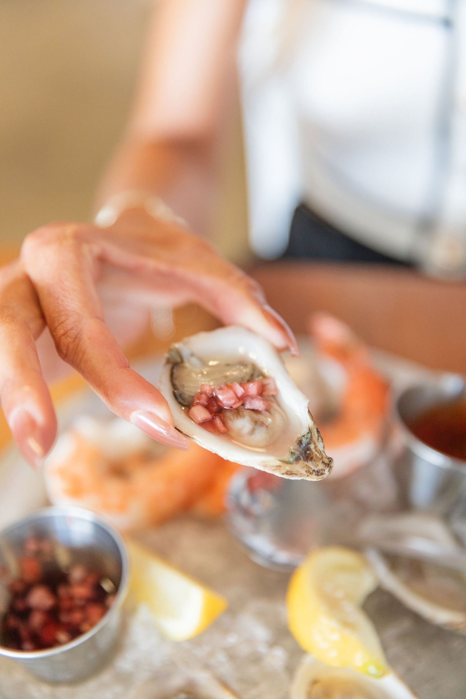 Fresh oyster being garnished with toppings and lemon wedges.