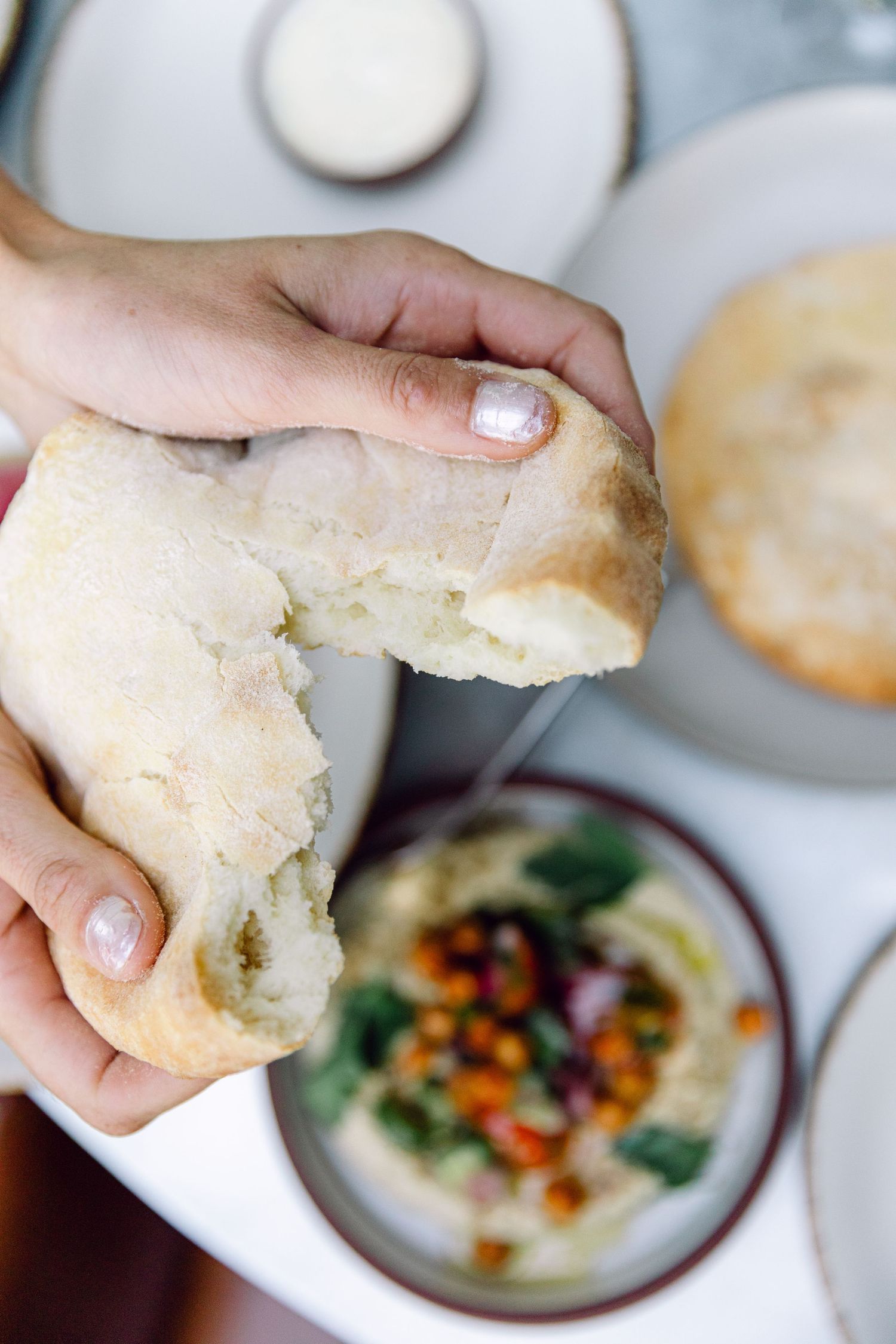 Fresh bread being torn apart over a colorful appetizer bowl.