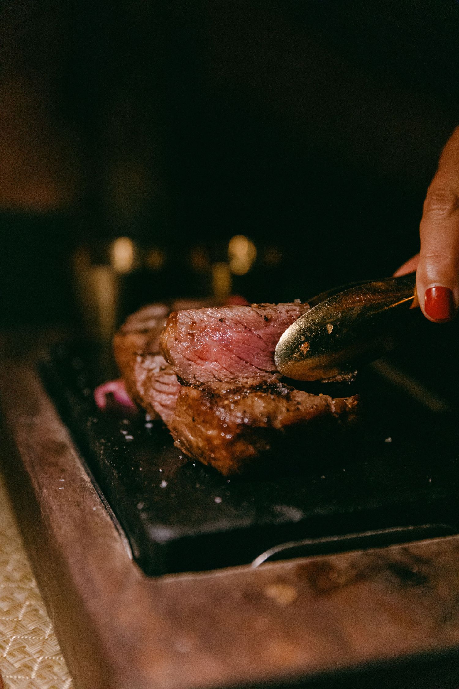 Medium-rare steak being cut on dark wooden board showing pink center.