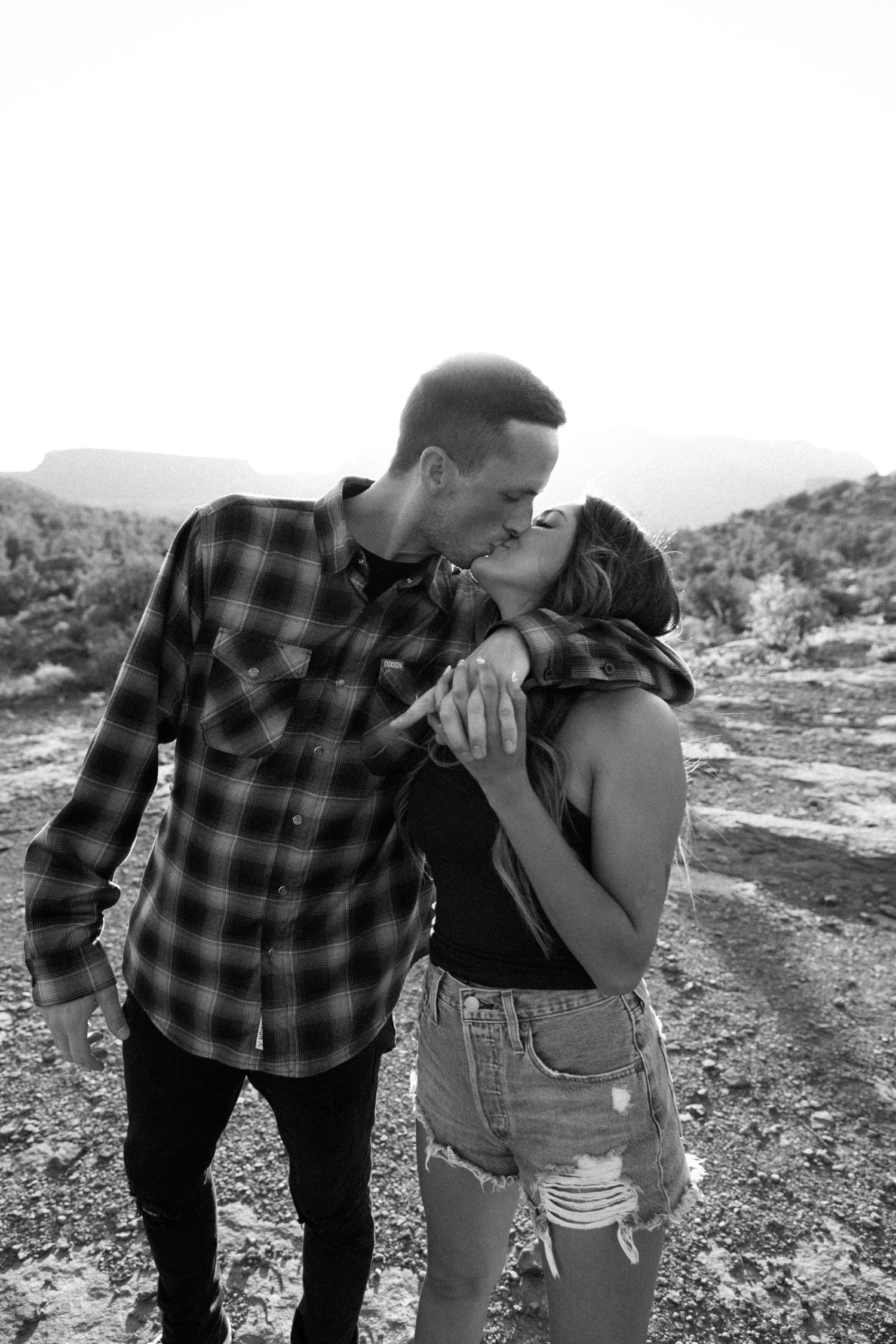 Couple in casual wear sharing tender moment against desert backdrop.