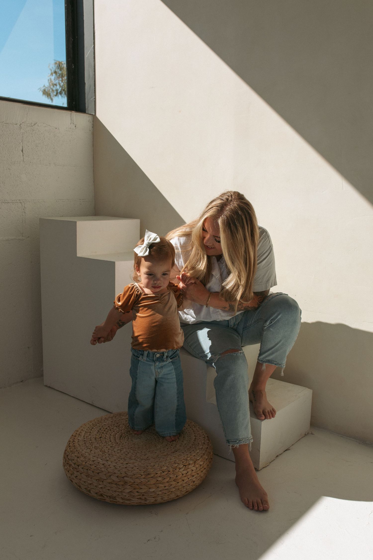 Parent and toddler share a sweet moment together on white steps near a window with dramatic natural lighting.