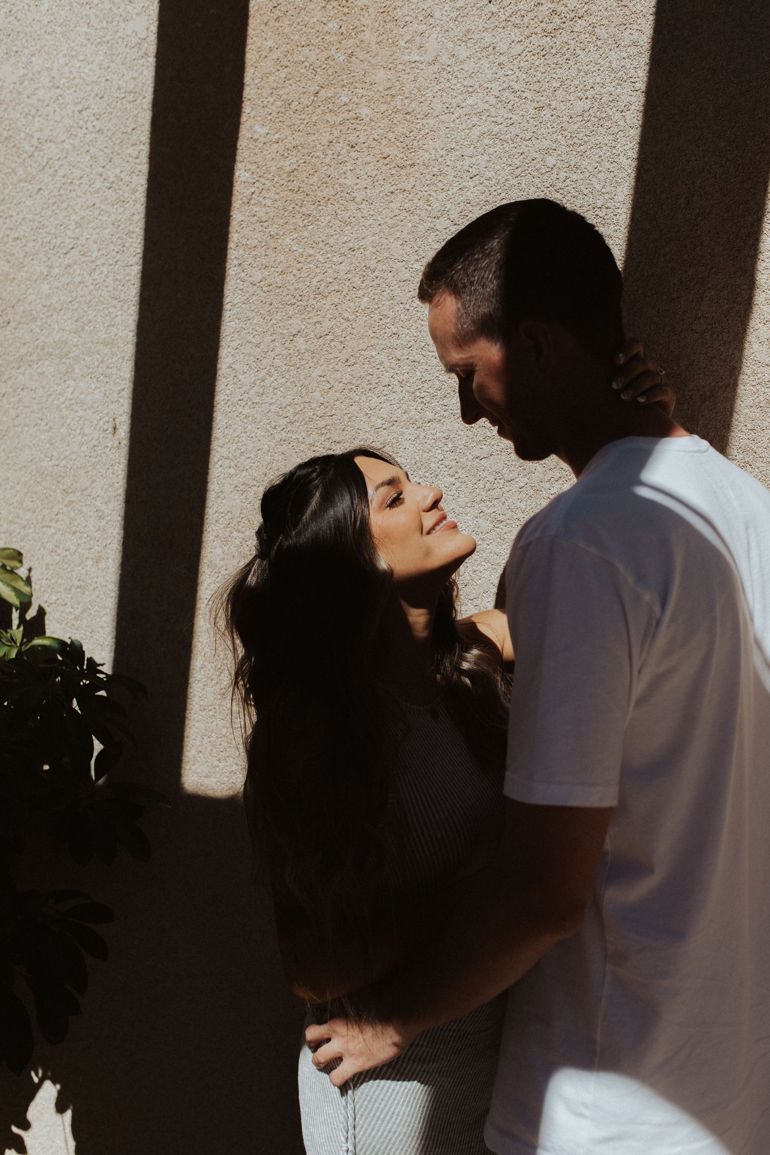 Intimate portrait of a couple against a white wall with dramatic shadows.