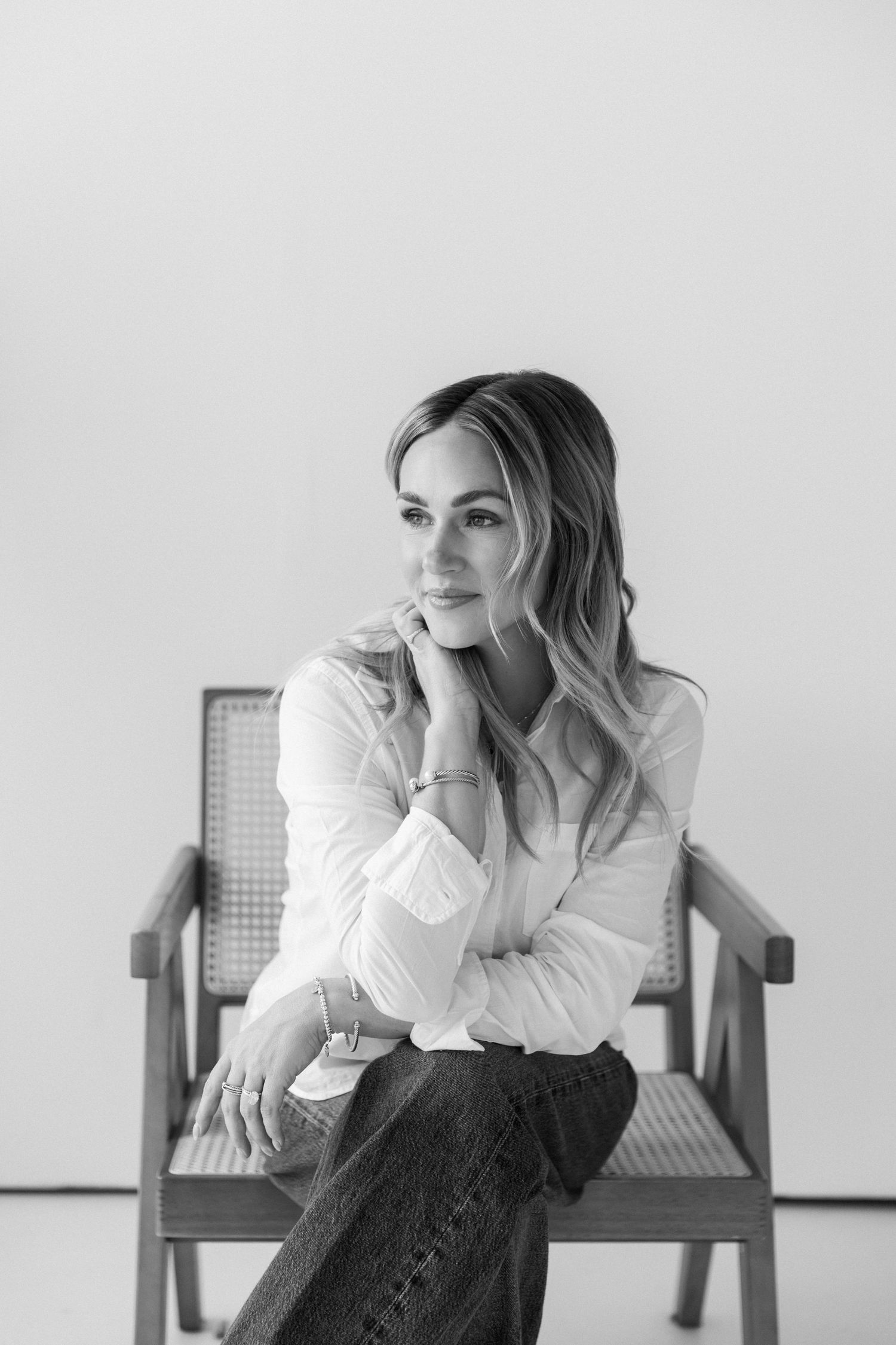 Black and white portrait of a woman in white shirt and jeans sitting gracefully in a wooden chair.
