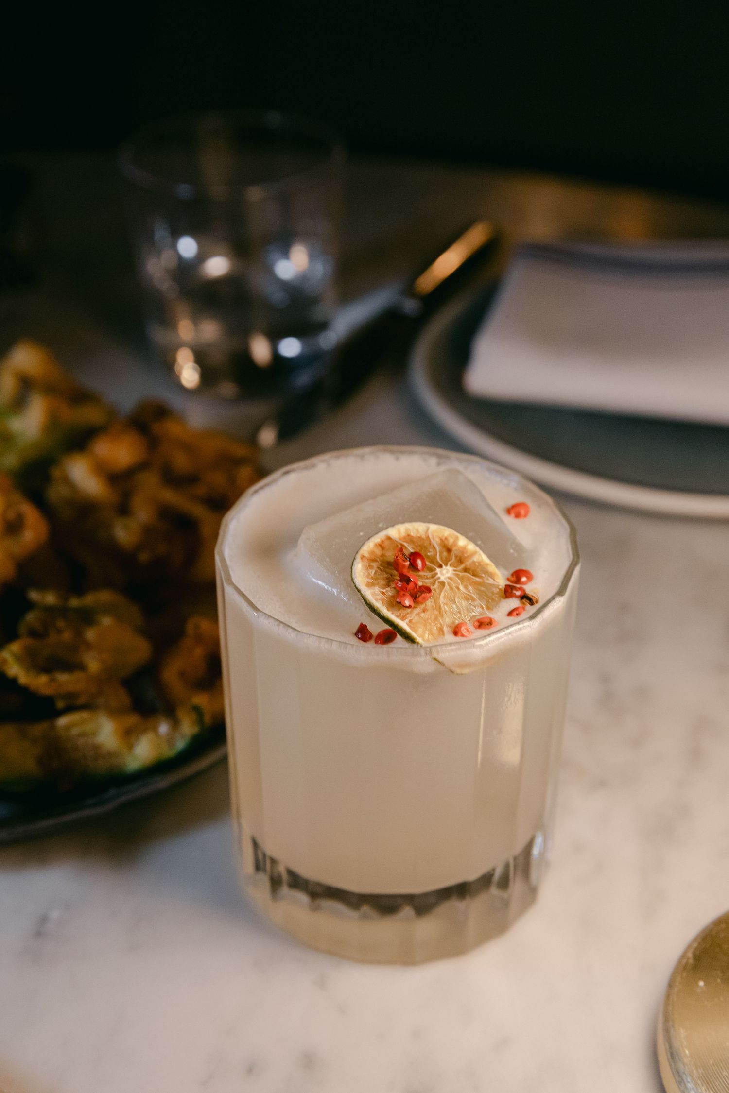 Frosted cocktail glass garnished with a dried citrus wheel and red garnish.
