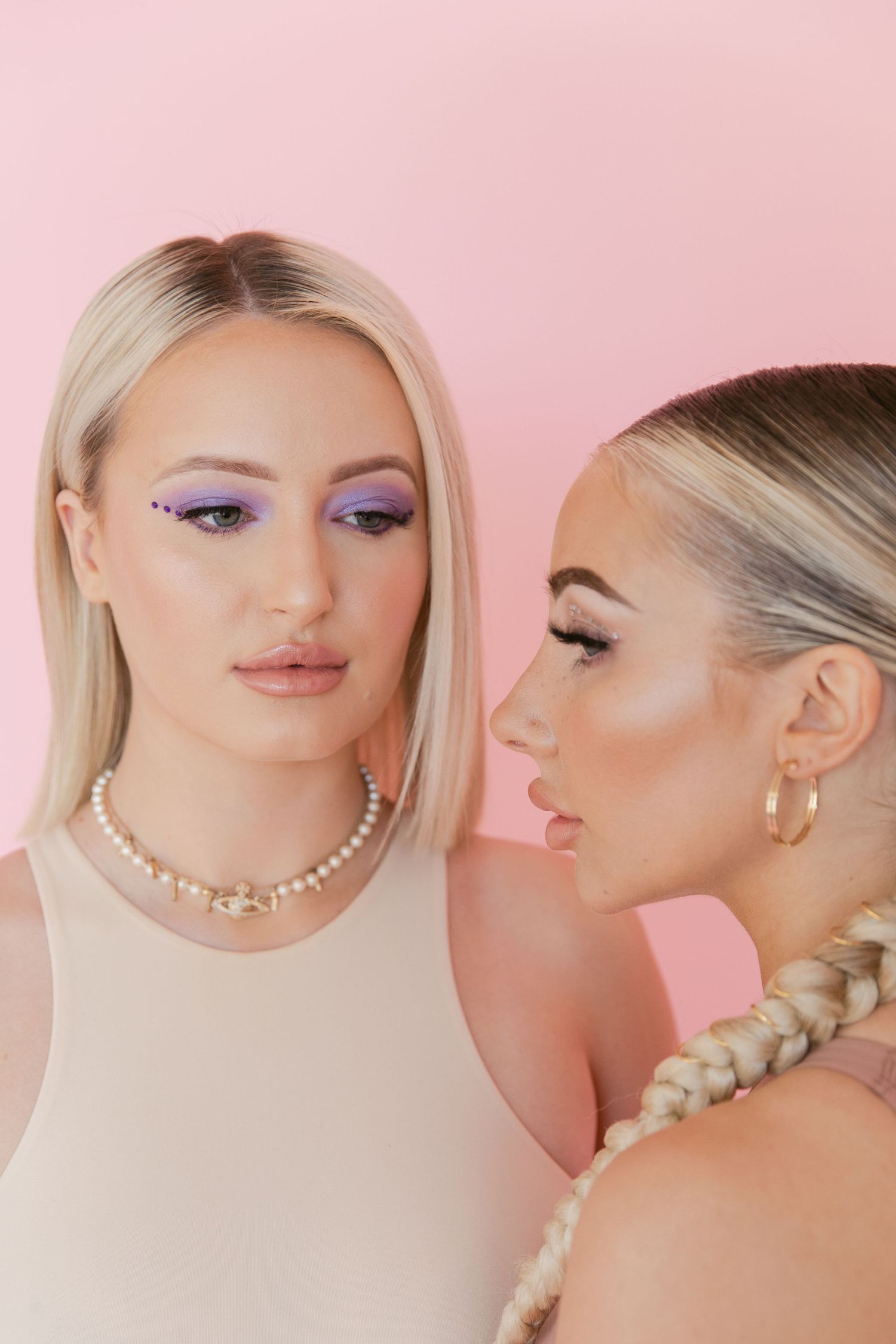 Close-up beauty shot of two models with pearl necklace and purple eyeshadow.