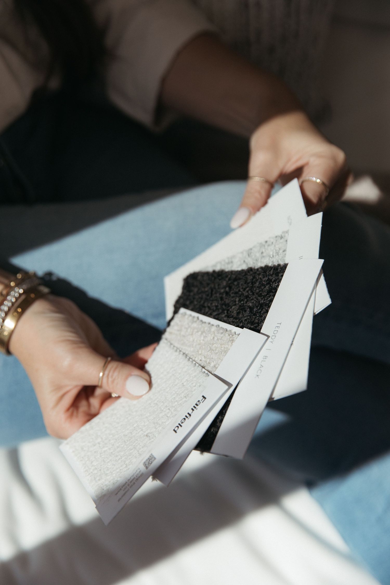 Hands holding fabric swatches and material samples in various shades and textures.