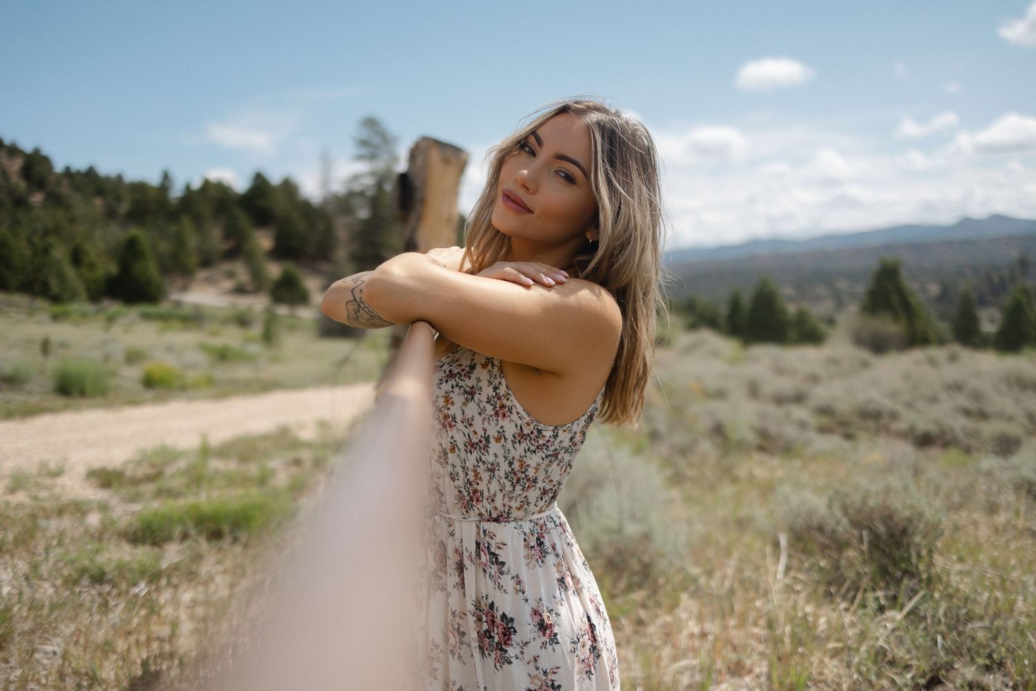 A person in a floral dress twirls joyfully in a scenic mountain meadow on a sunny summer day.