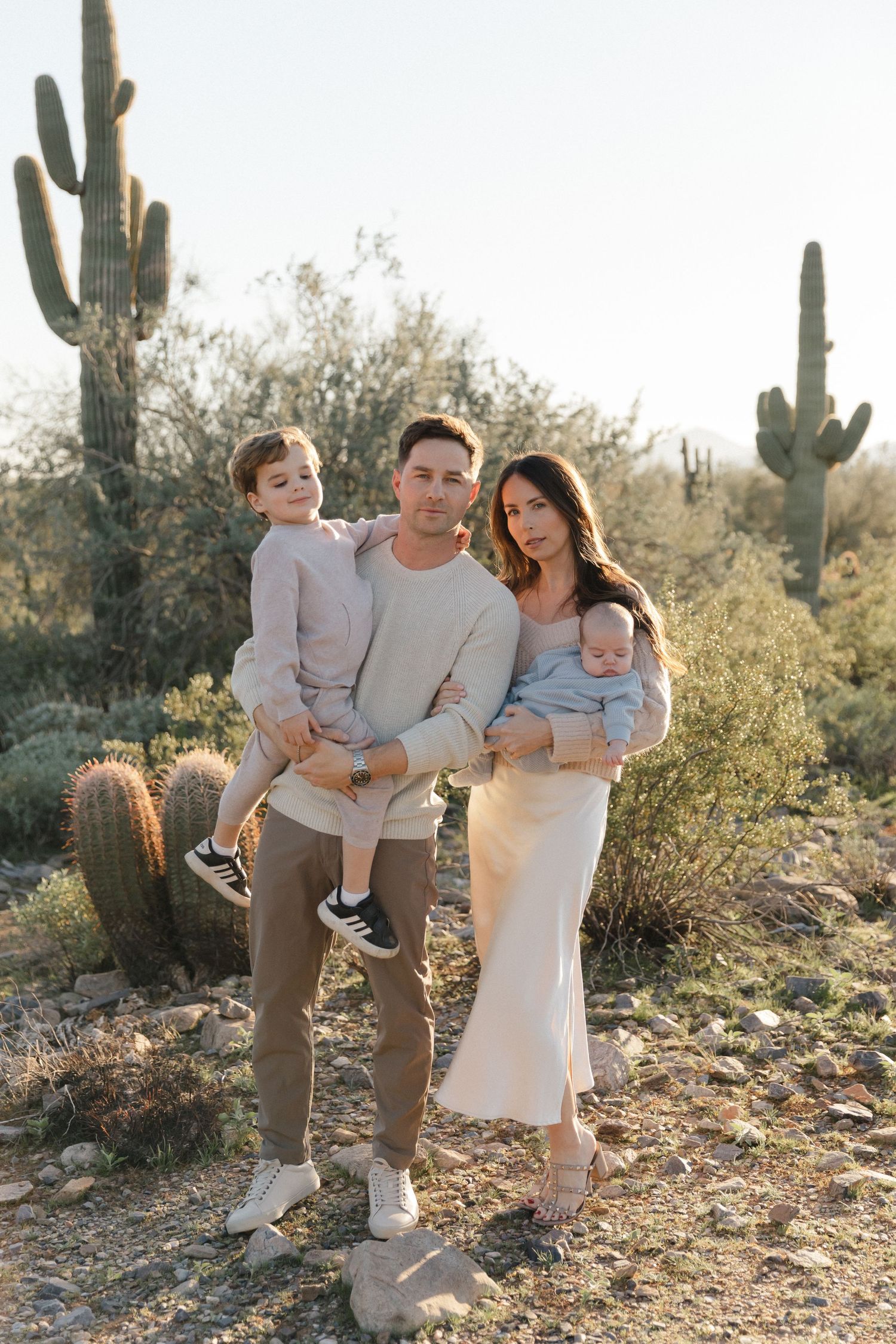 A family poses together in a desert landscape with tall saguaro cacti at sunset.