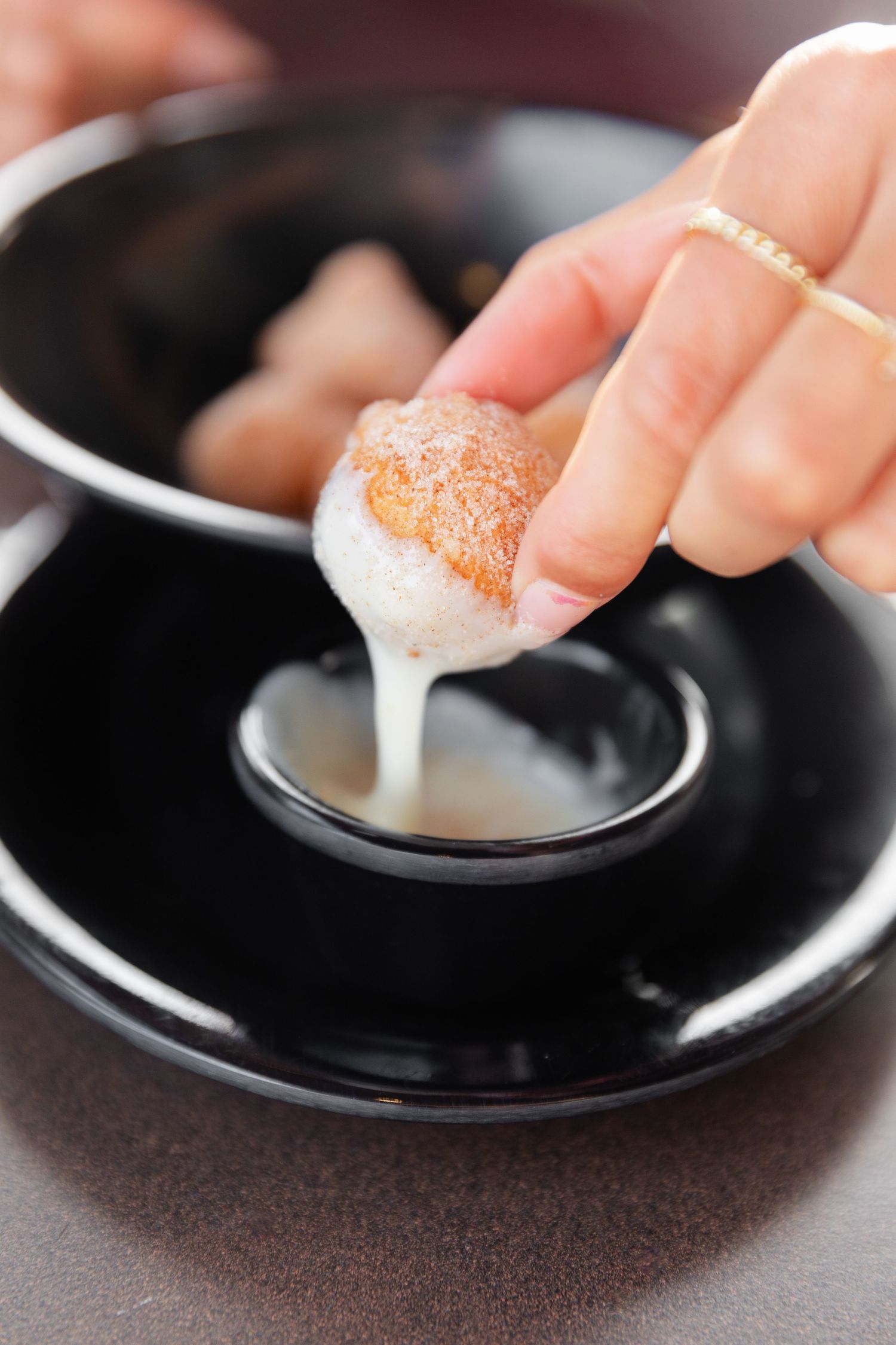 Close-up of dipping sauce with hand holding food over black ceramic dish.