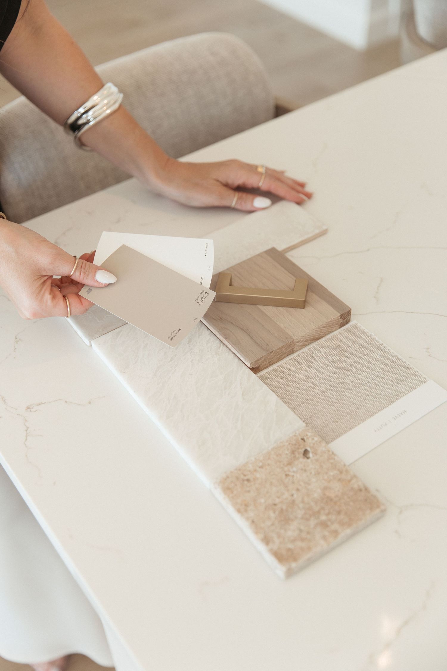 Hands arranging neutral color material swatches on white surface.