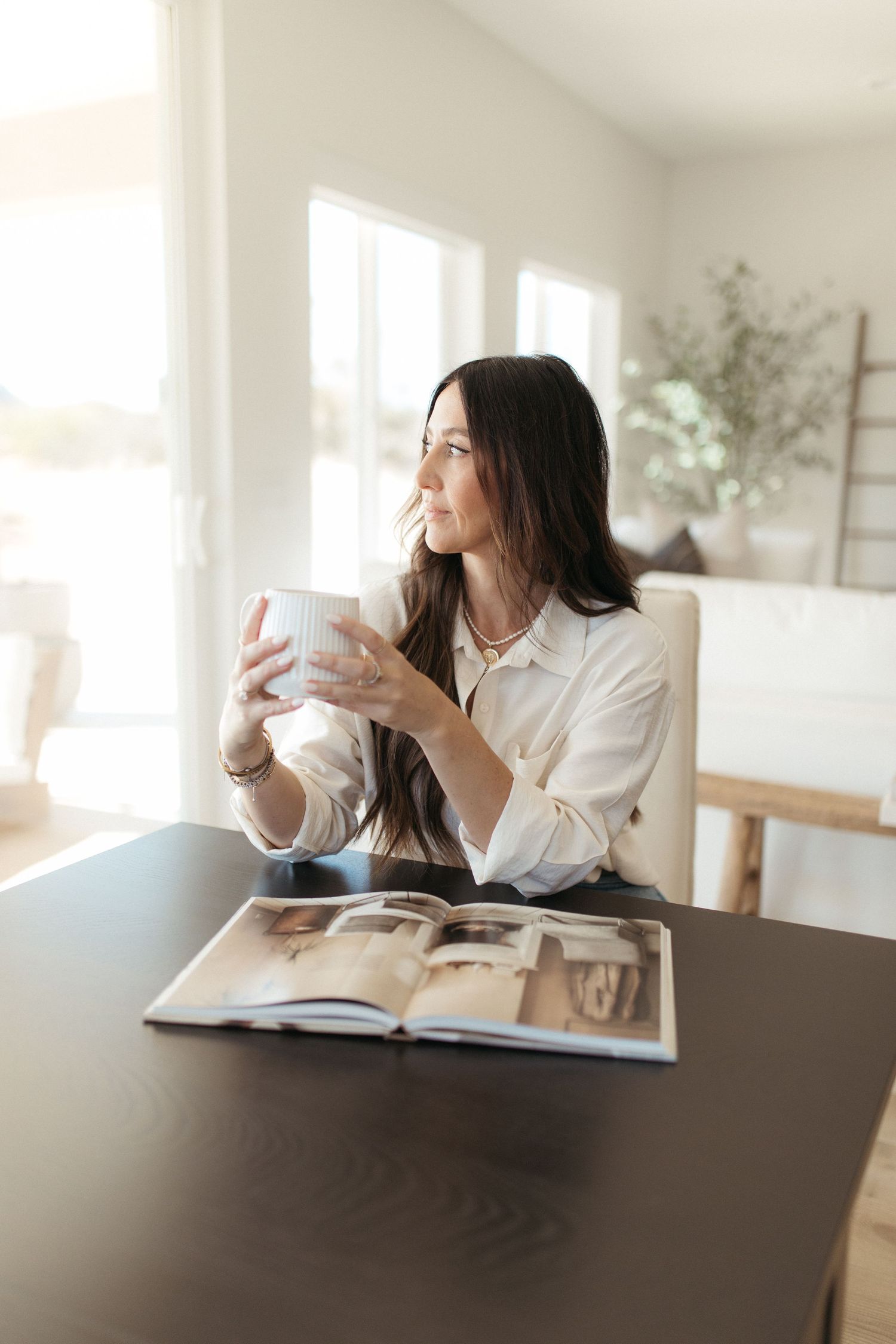 Woman enjoying coffee while reading magazine in bright modern interior.