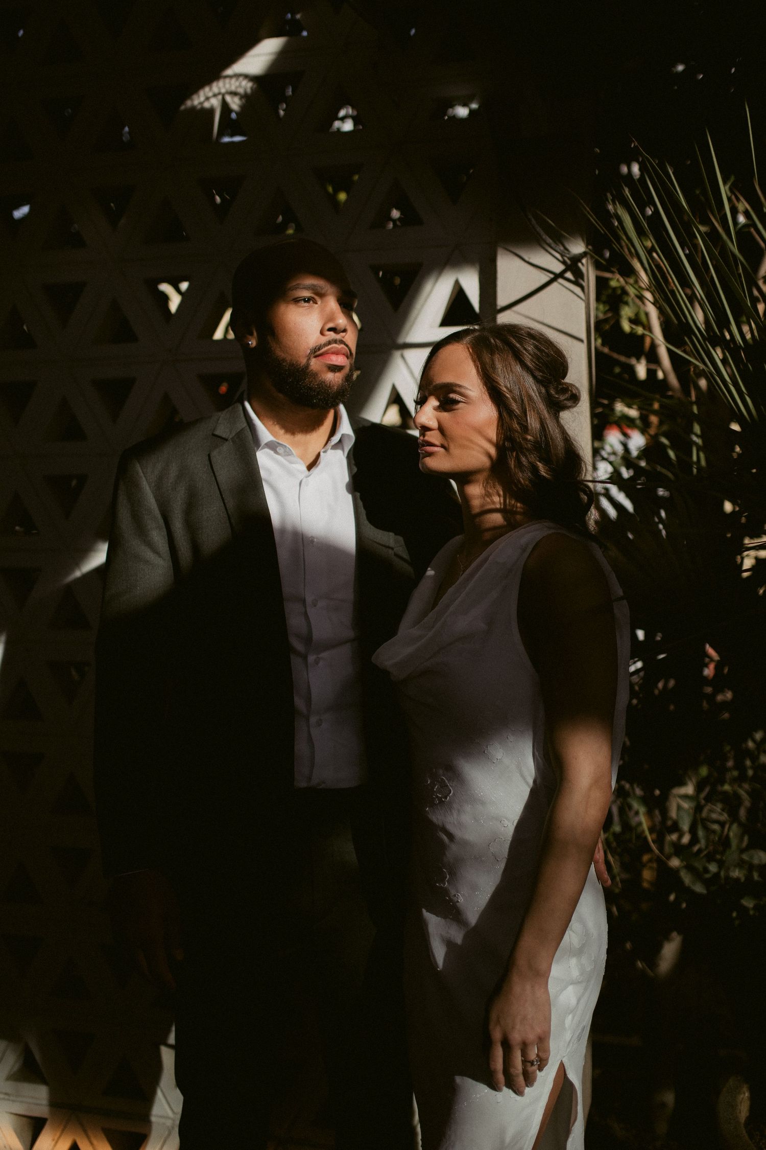 A romantic moody portrait of a couple in formal attire standing against a dark background with dramatic lighting.