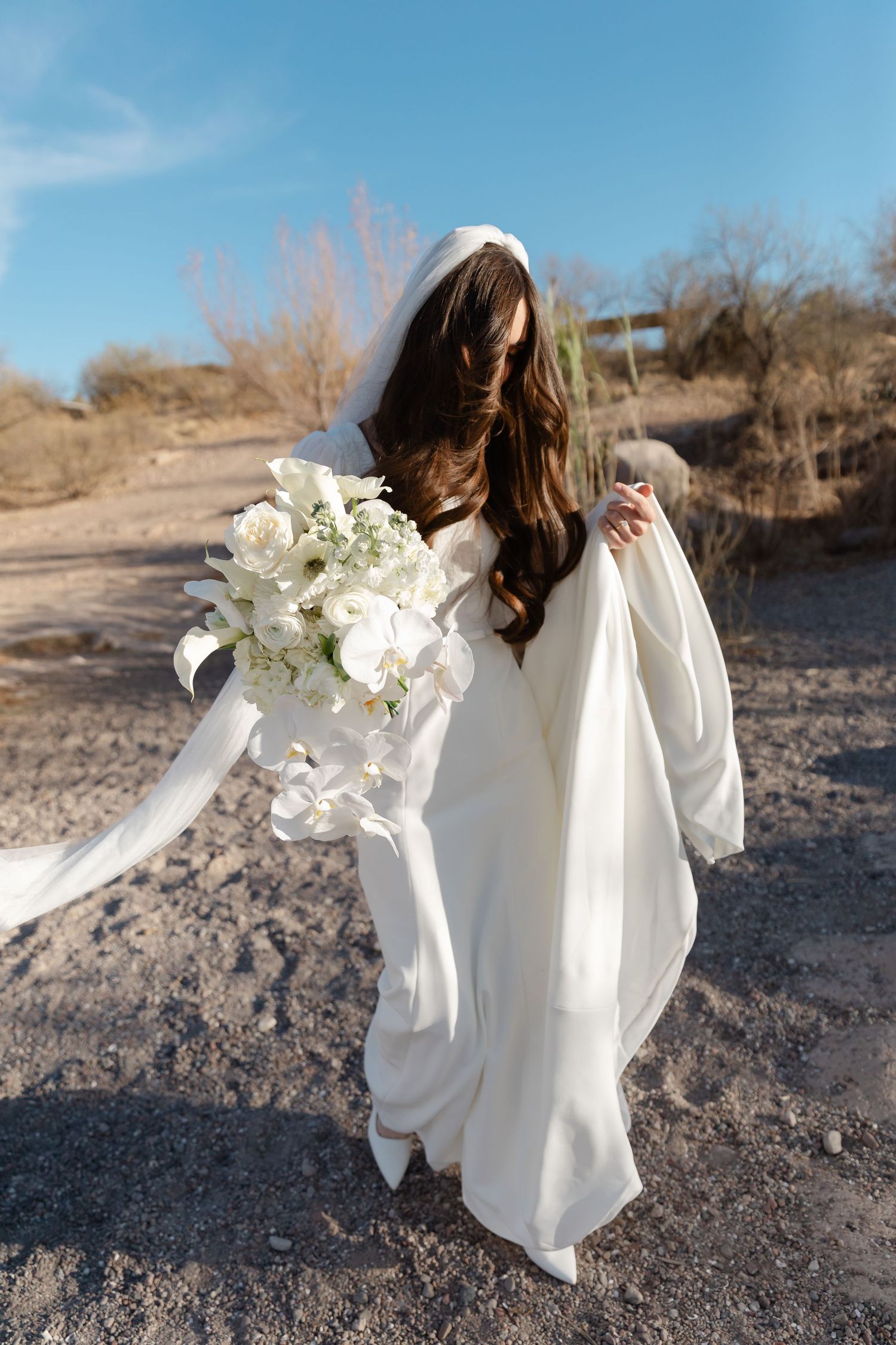 A figure in a flowing white dress dances gracefully in a desert landscape with white flowers in hand.