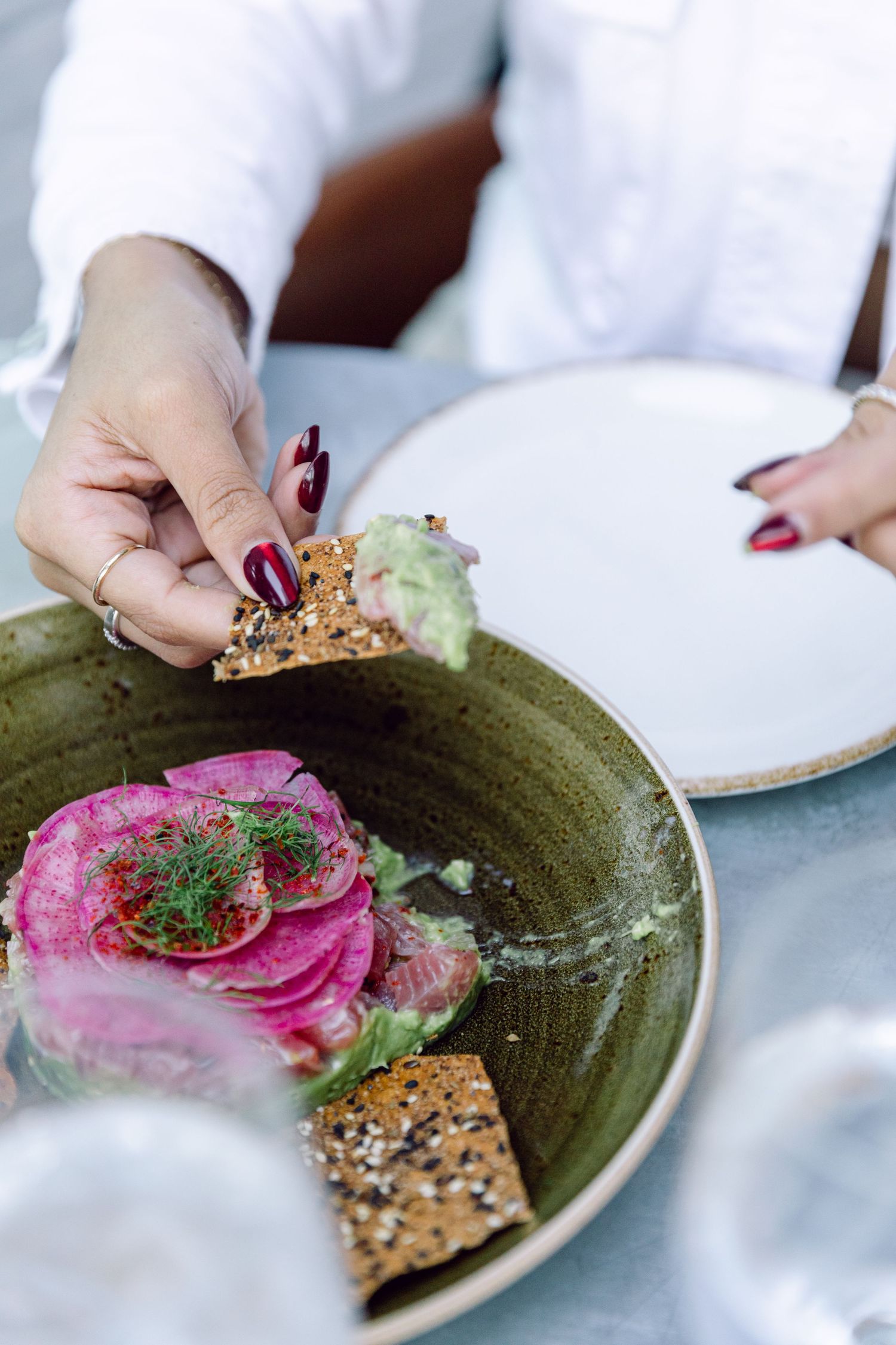 Close-up of a gourmet appetizer with pink radish and fresh herbs on a green ceramic plate.