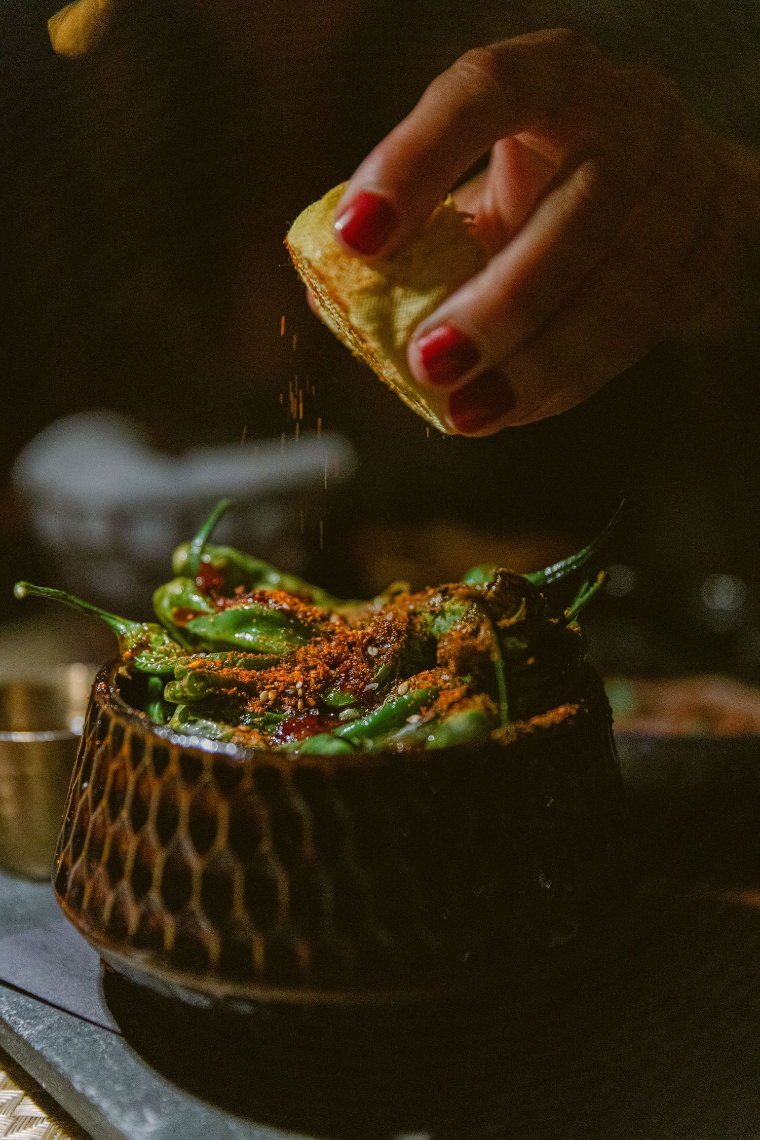 Hand squeezing lemon over green beans in a textured ceramic bowl.