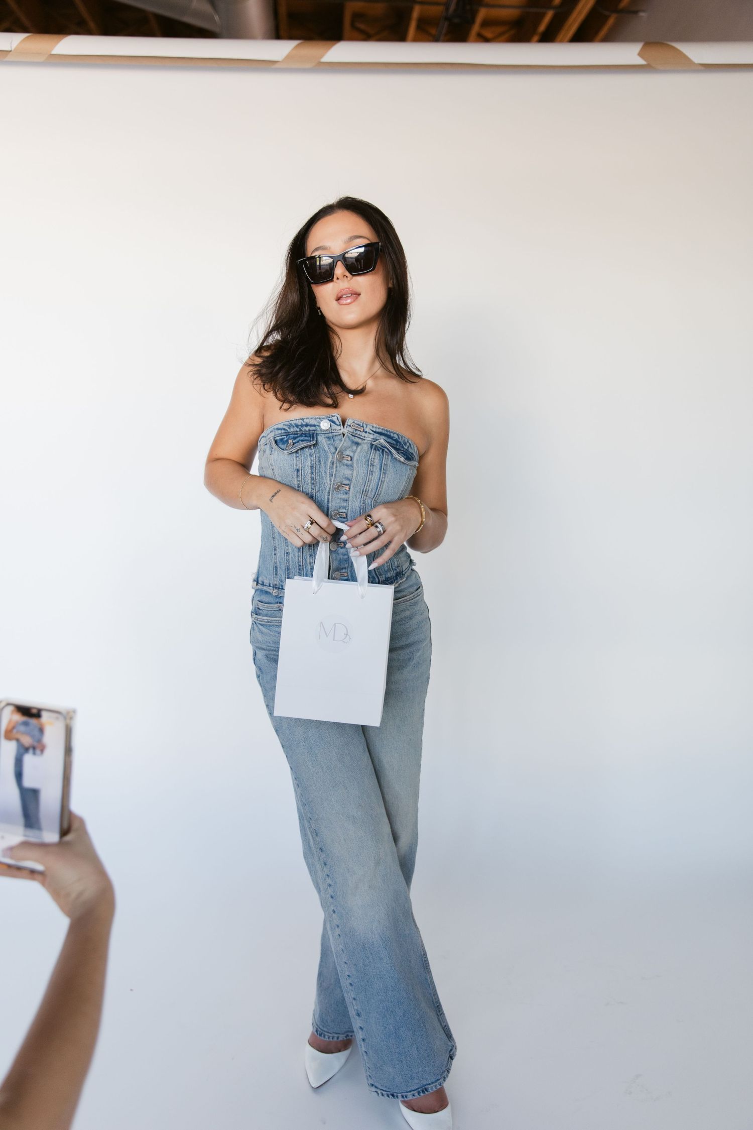 Fashion model in denim holding a white shopping bag against plain wall.