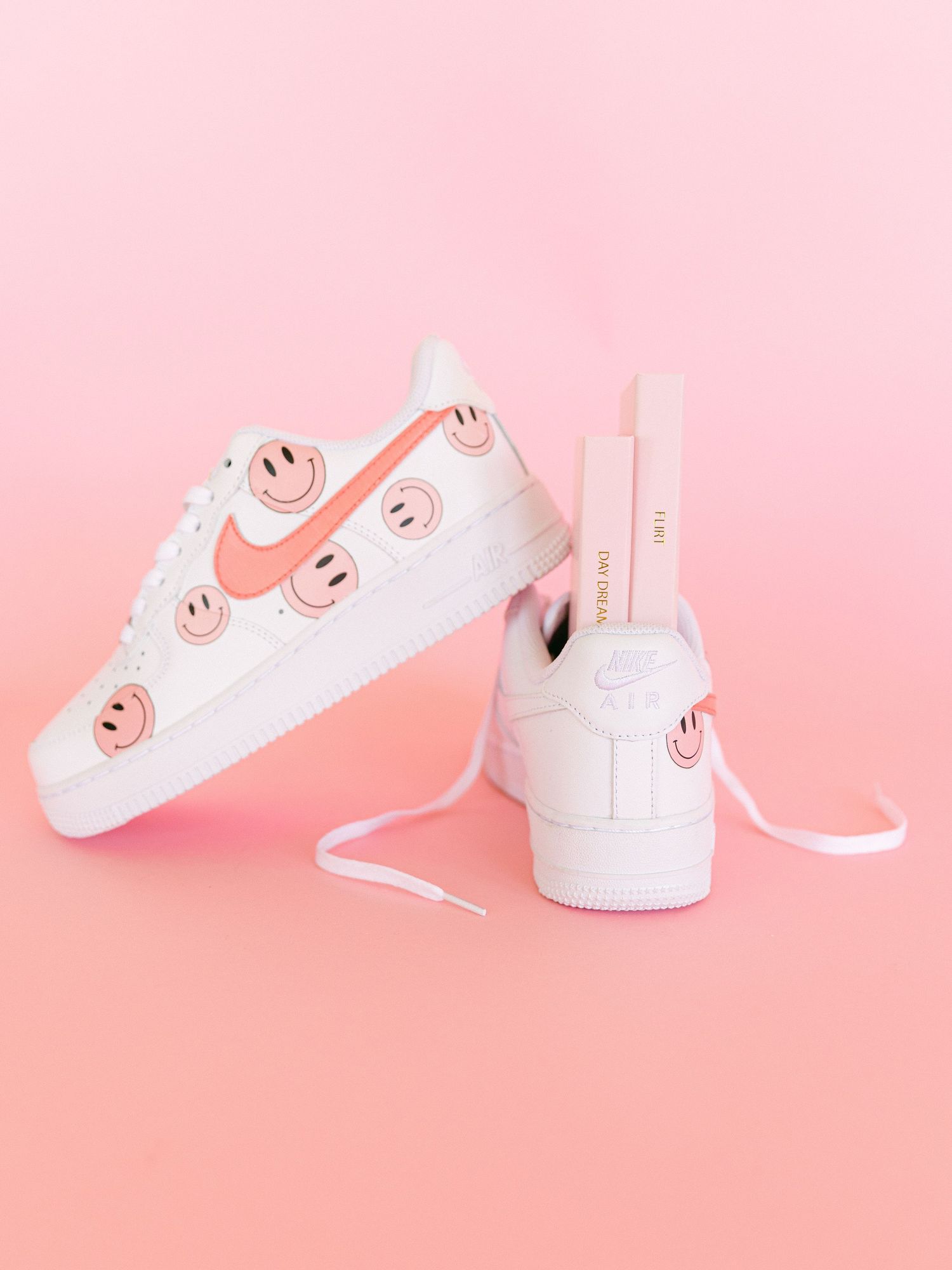 White sneakers with pink accents and shoelaces styled on pink background.