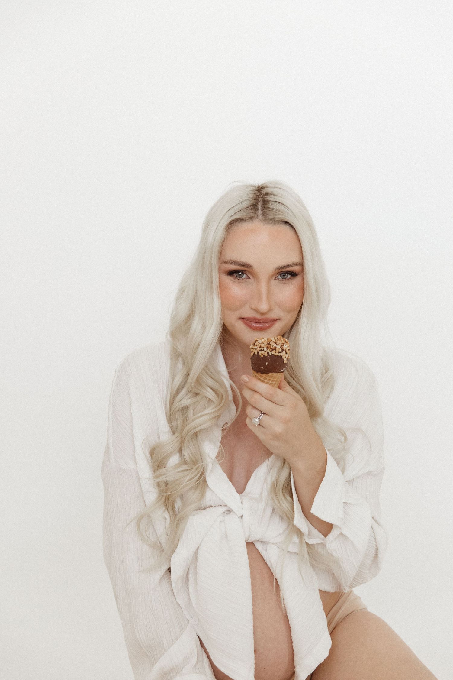 Maternity boudoir photo with subject holding chocolate bar in white button-down shirt.