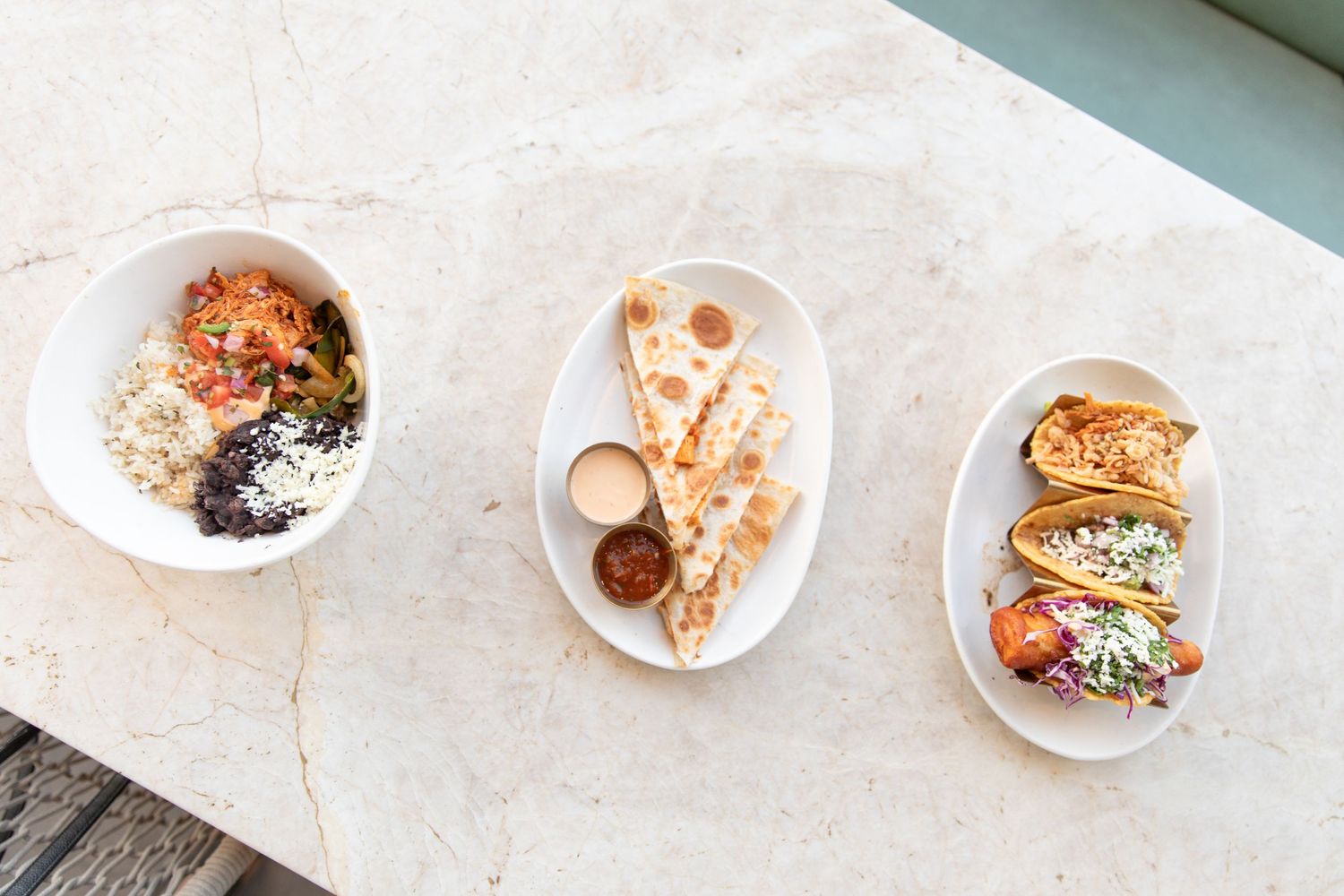 Overhead view of three white plates with various appetizers and dishes on marble surface.