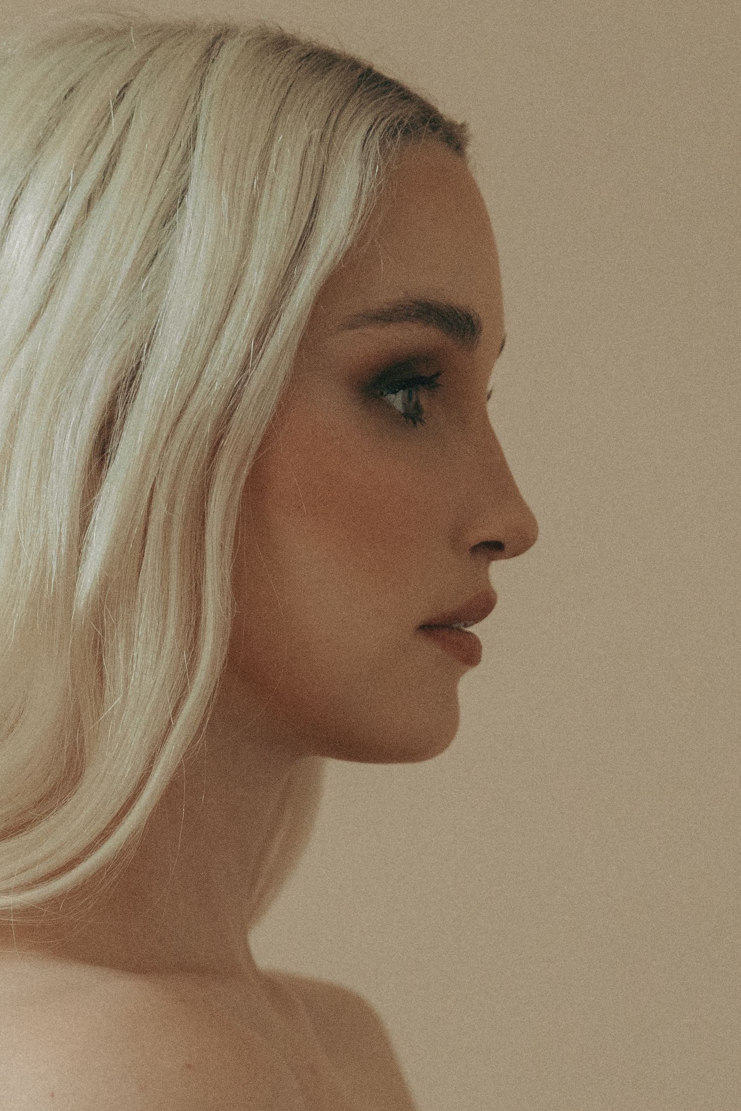 Profile portrait against neutral background showcasing platinum blonde hair and makeup.
