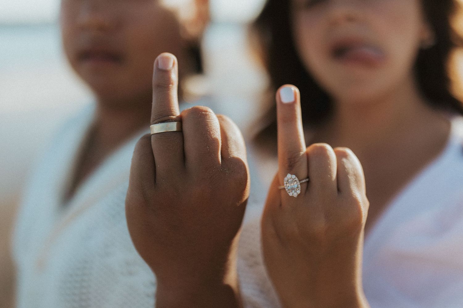 Close up of hands showing engagement ring and middle finger gesture.