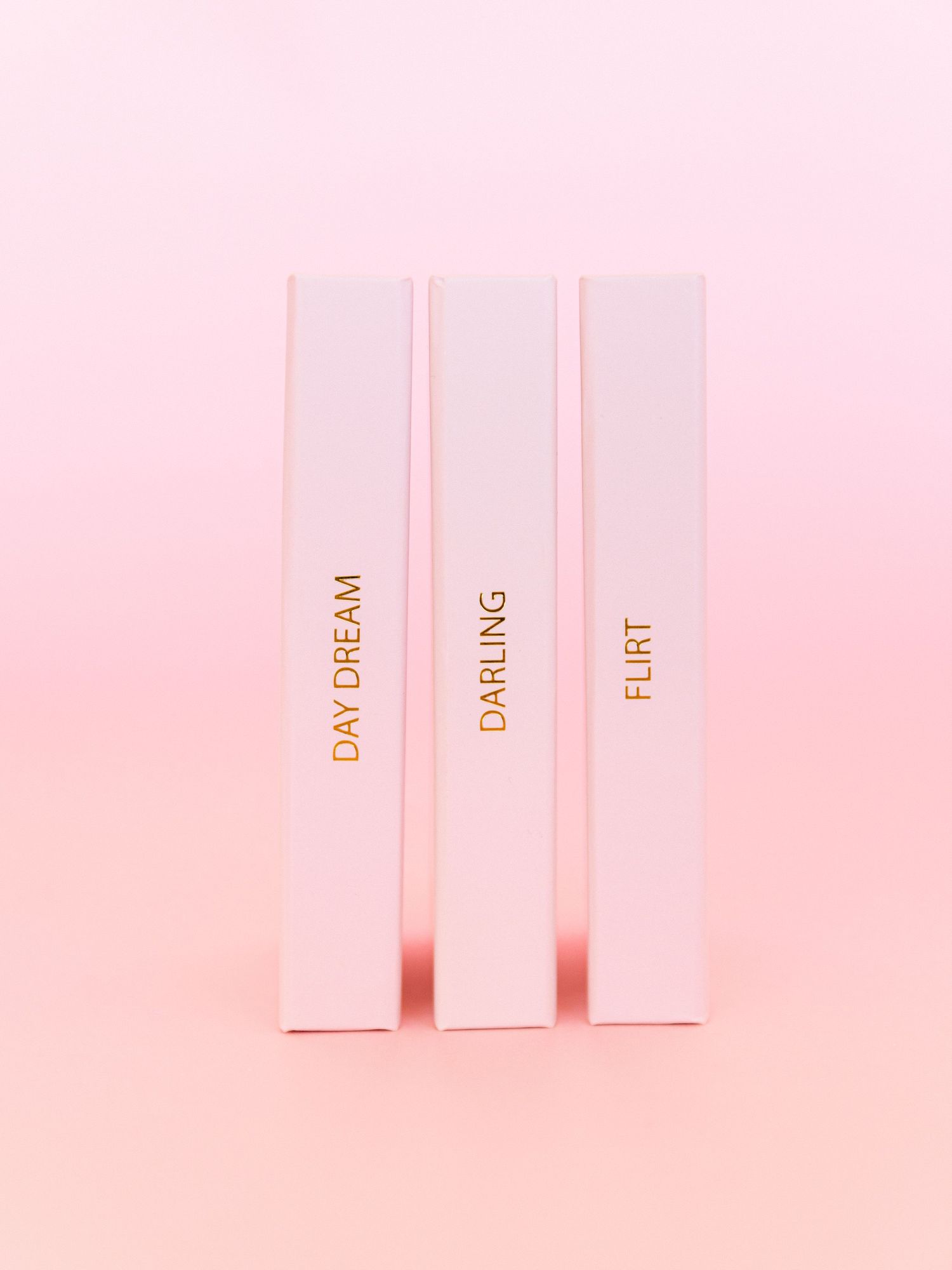 Three pink book spines with gold text reading 'Day Dream', 'Darling', and 'Flirt' against pink background.