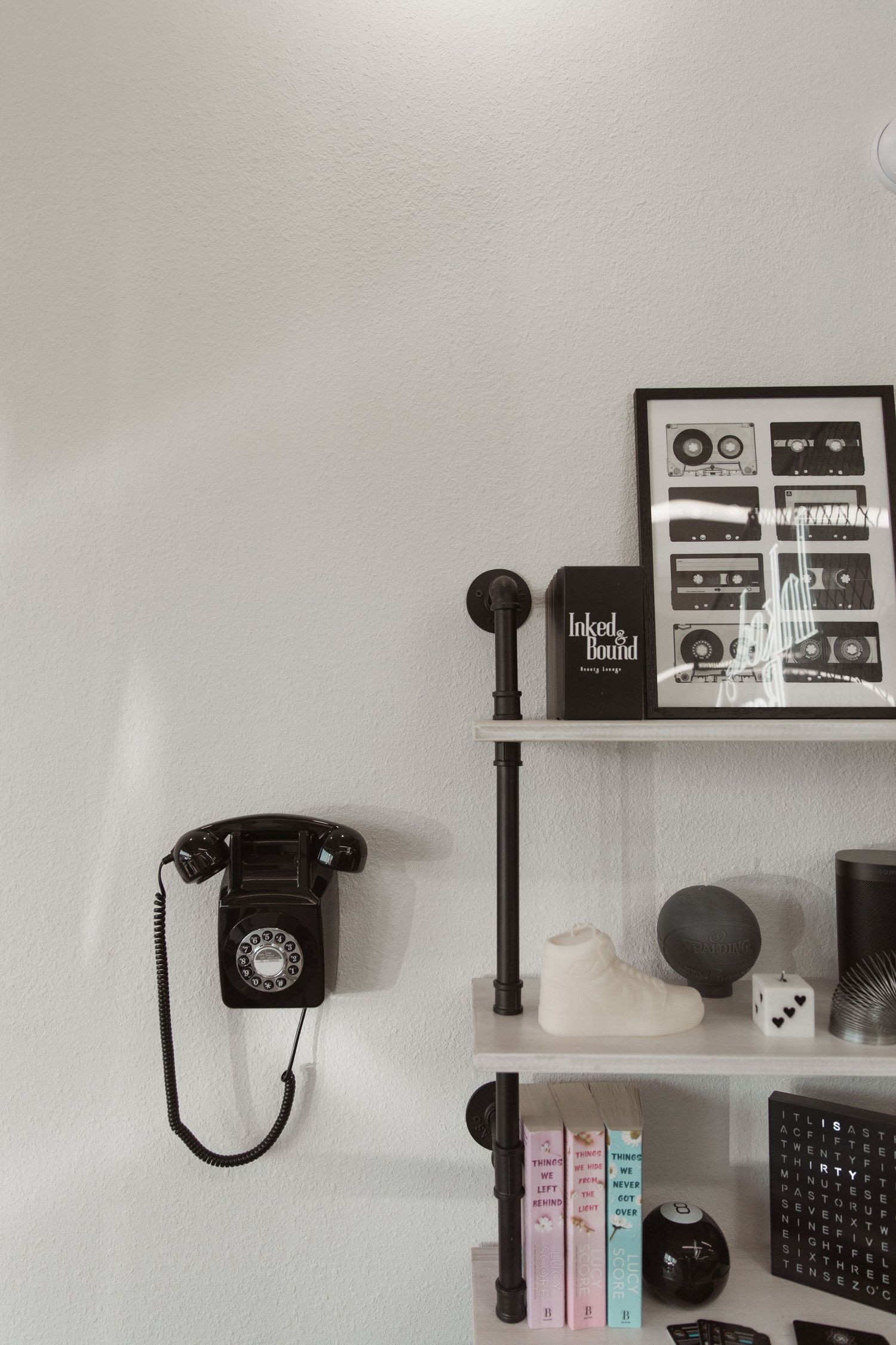 Vintage black rotary phone on wall with framed artwork and decorative shelving.
