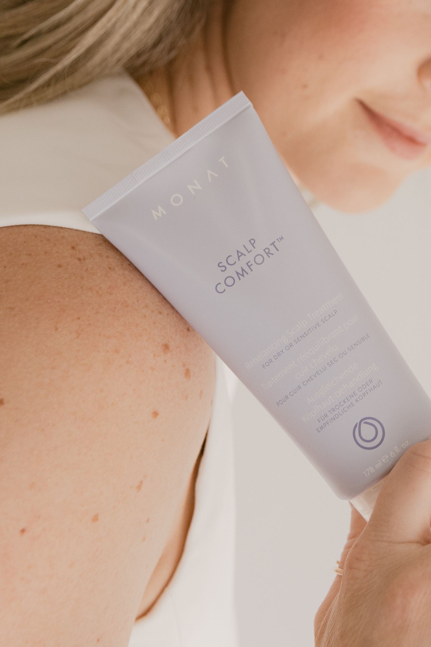 Woman holding MONAT Scalp Comfort cream tube, showcasing the light purple hair care product packaging.